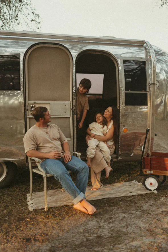 Family sitting outside of airstream trailer and smiling at each other