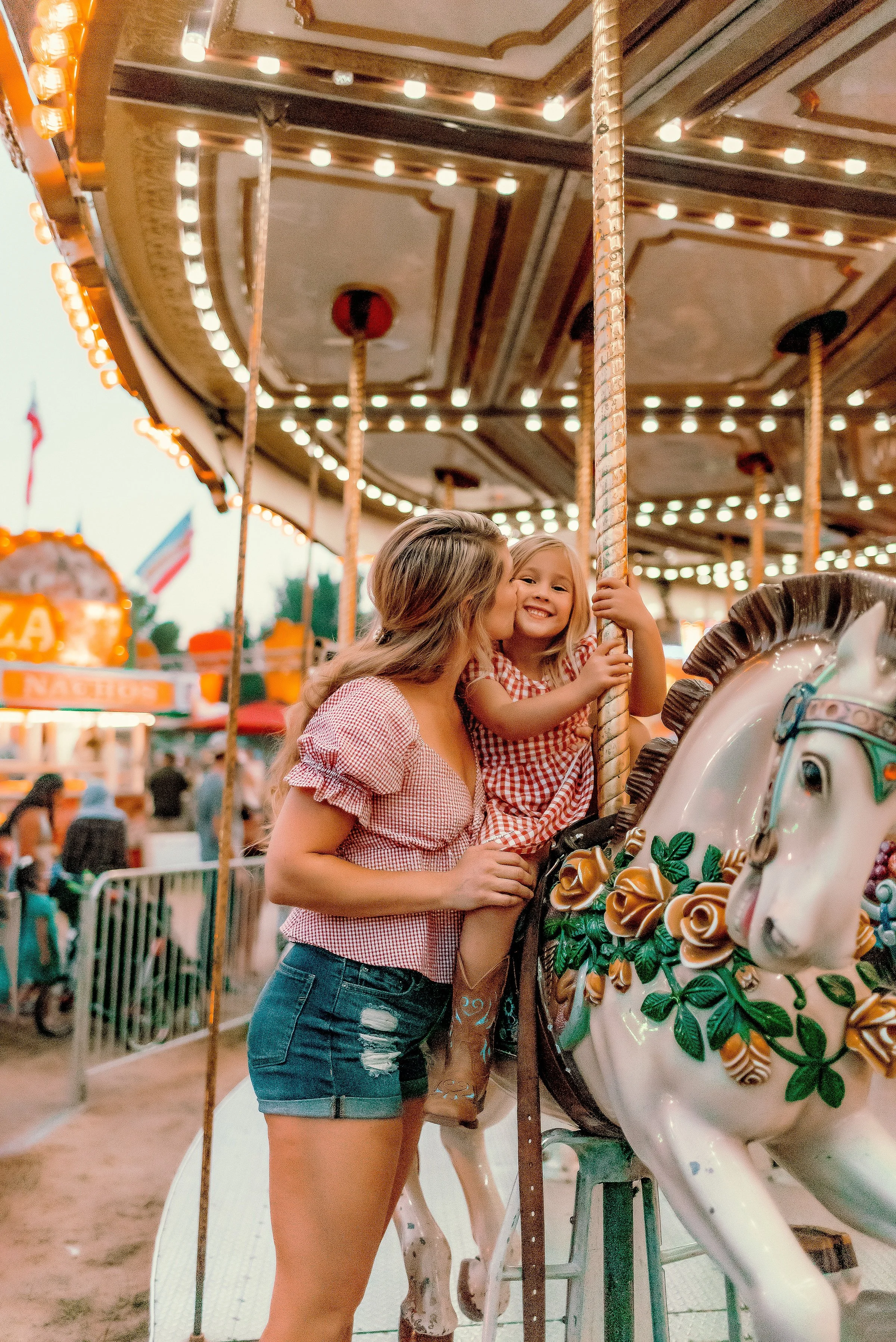 Mother kissing daughter on cheek while she rides on the carousel at the county fair