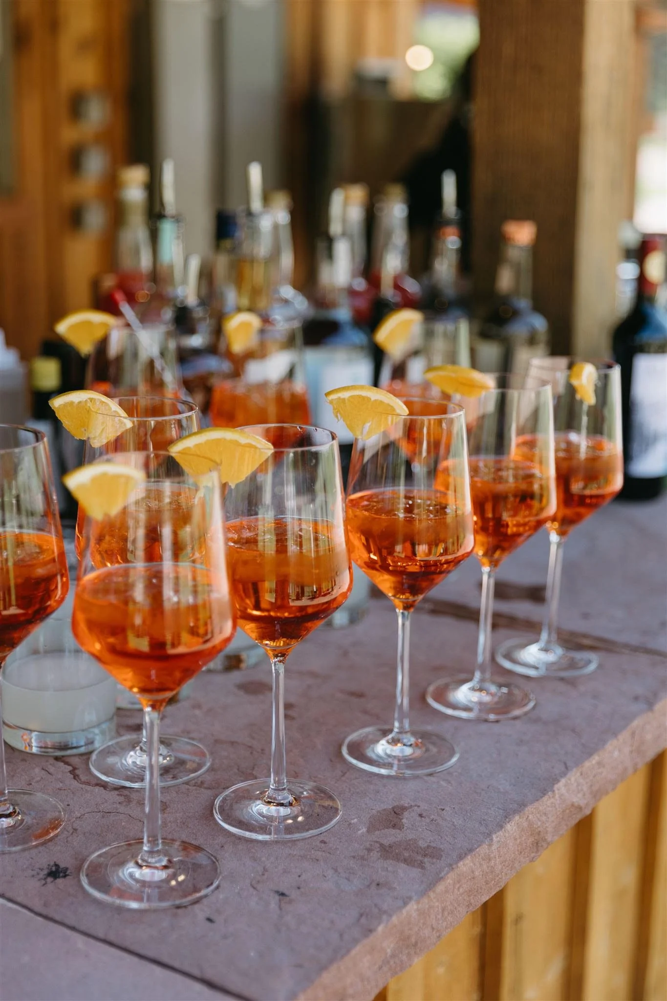 Row of glasses filled with orange-colored drink garnished with lemon wedges, set on a bar counter at a wedding at Planet Bluegrass.
