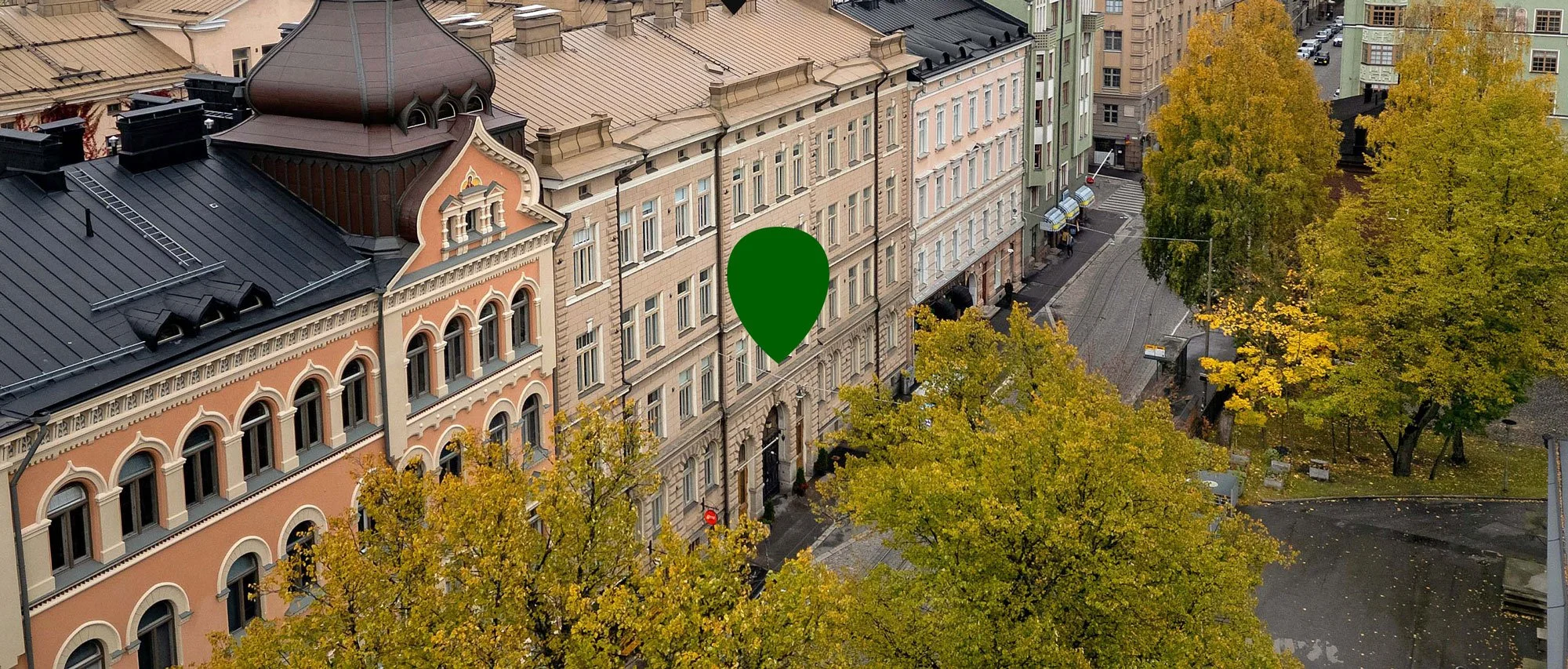 Kuvassa on kaupunkinäkymä katolta, jossa näkyy historiallisia rakennuksia ja puutalojen kattoja. Etualalla on keltaisia ja vihreitä lehtiä pudonneina maahan.