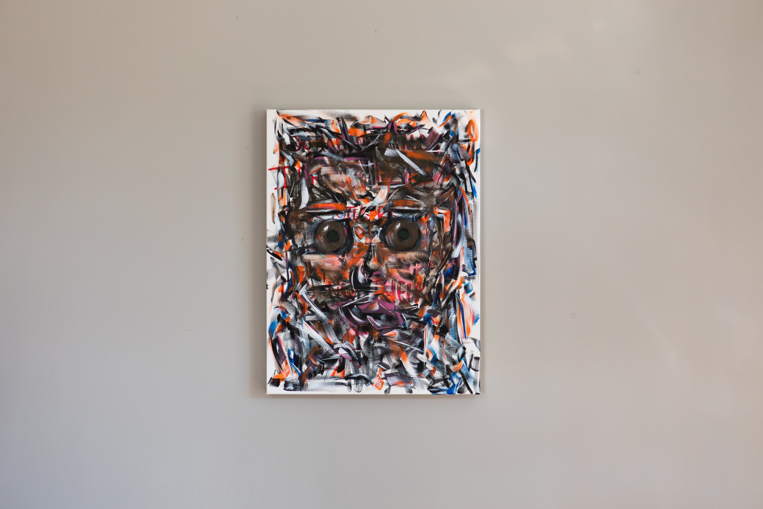 An abstract painting with vibrant strokes of black, orange, pink, blue, and white on a vertical canvas, hung on a plain gray wall.