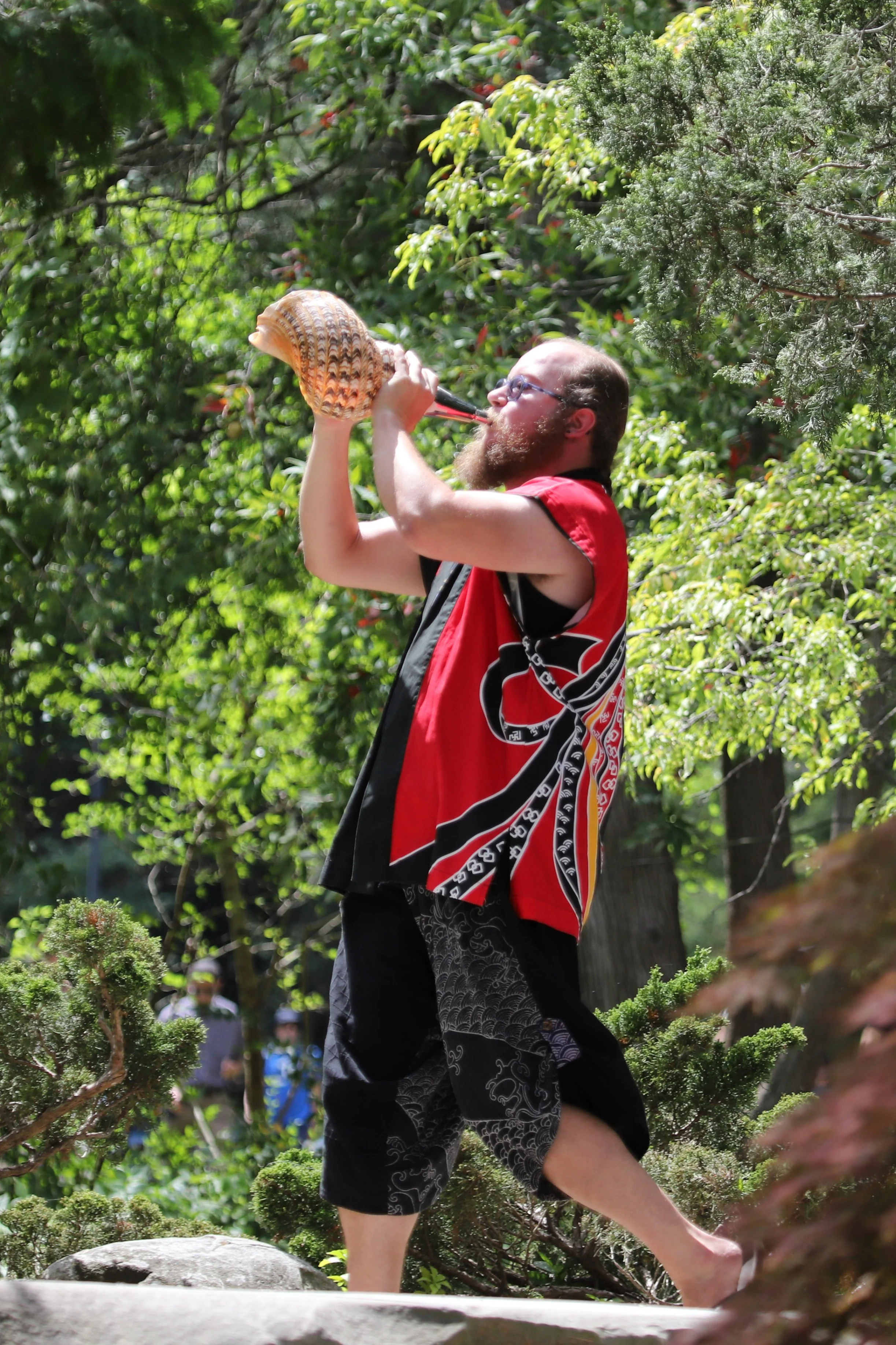 person blowing a large shell in a summer garden wearing festive red happi