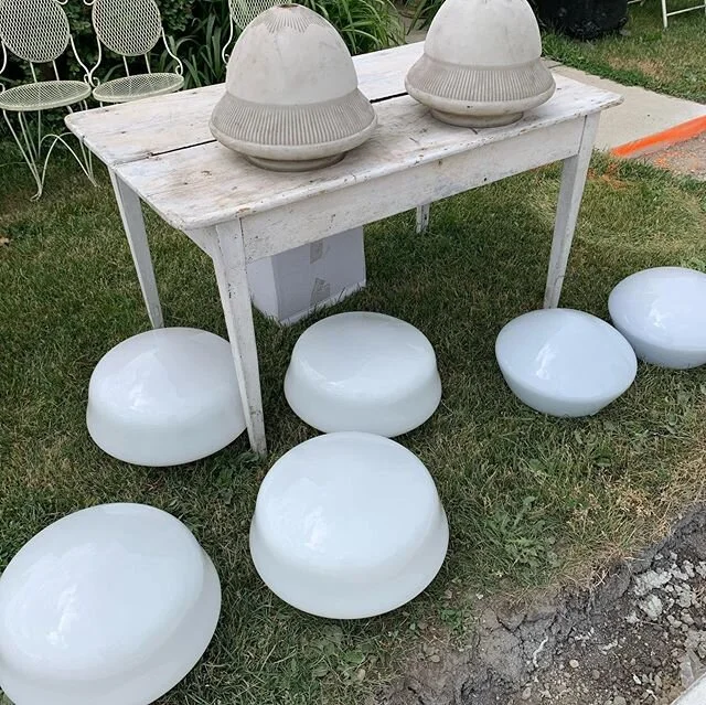 Milk glass lamp globes and mounts dating between 1920-40. These were salvaged from the Masonic Hall in Stratford Ont.  There are a set of four matching shades and three additional pairs as well. The earliest pair of globes are sitting on white table.