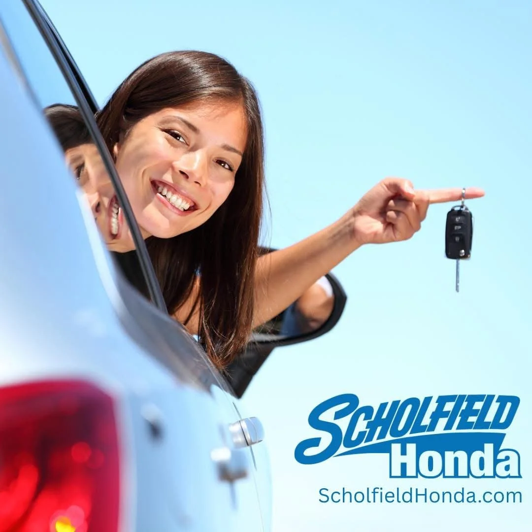 A woman smiling, leaning out of a silver car window, holding a car key with a remote in her right hand, against a light blue sky background, with the text 'Scholfield Honda' and the website 'ScholfieldHonda.com'.