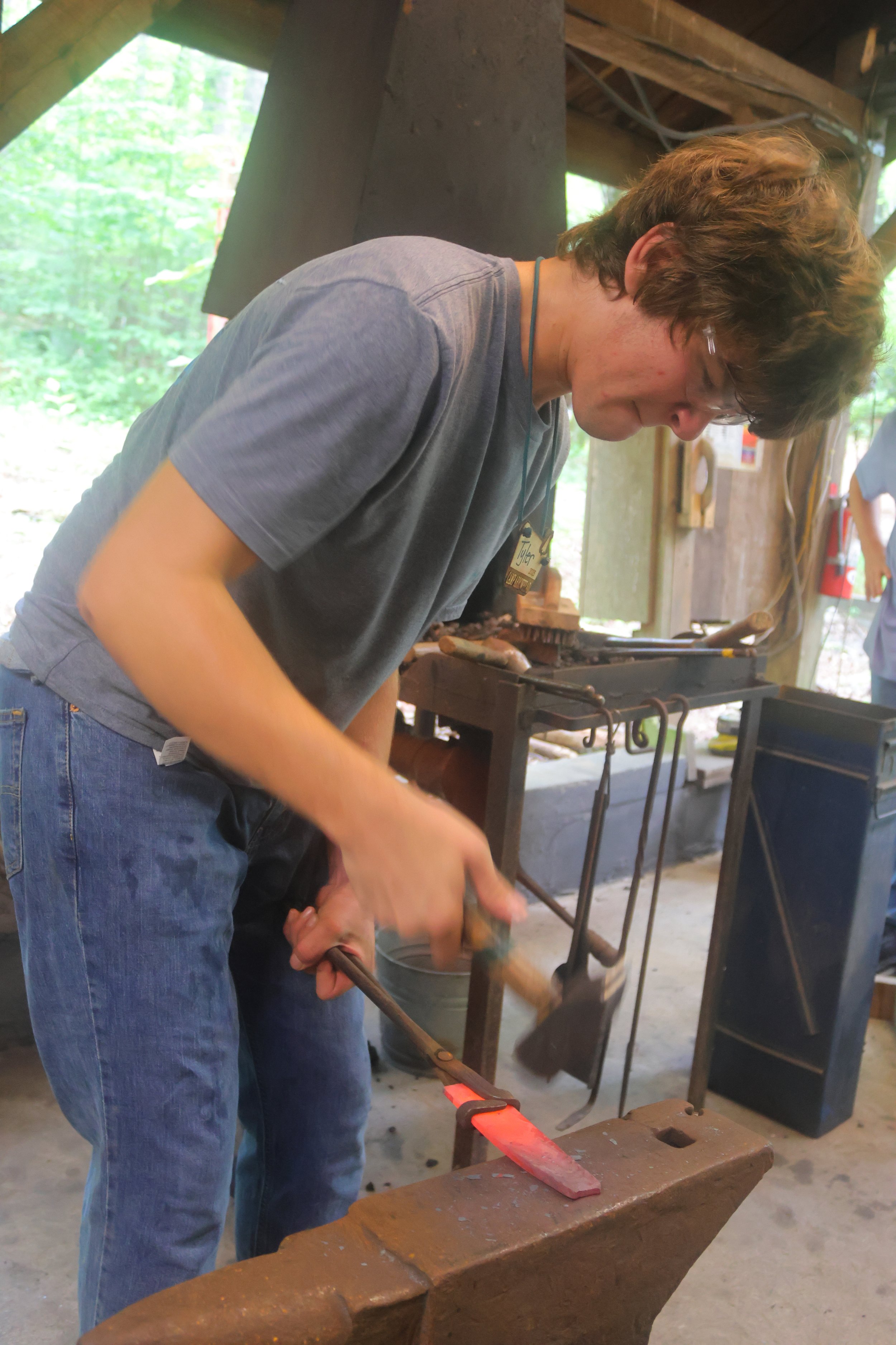 Young Maker at anvil hammering his Arrowhead at Camp.