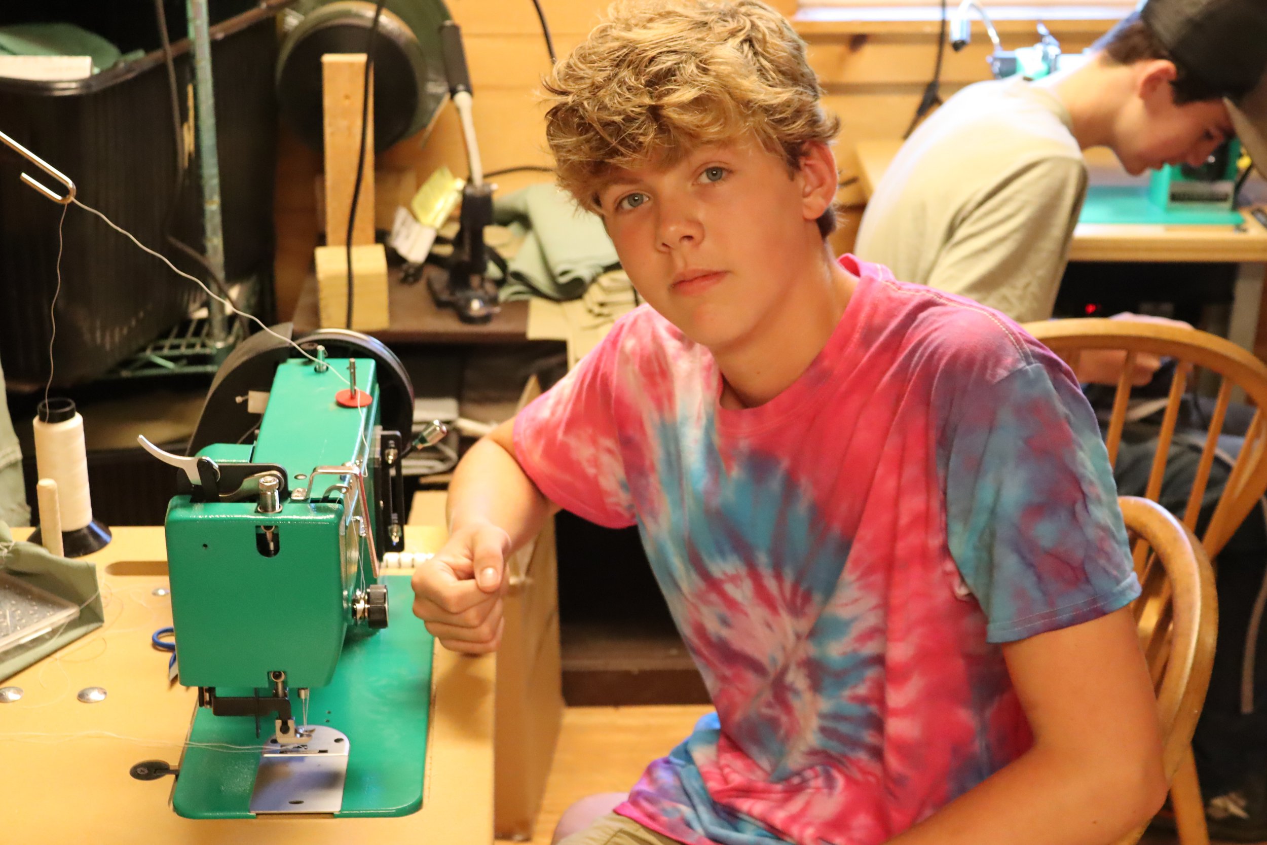 Camper pausing his sewing to pose in front of the machine at Camp. 