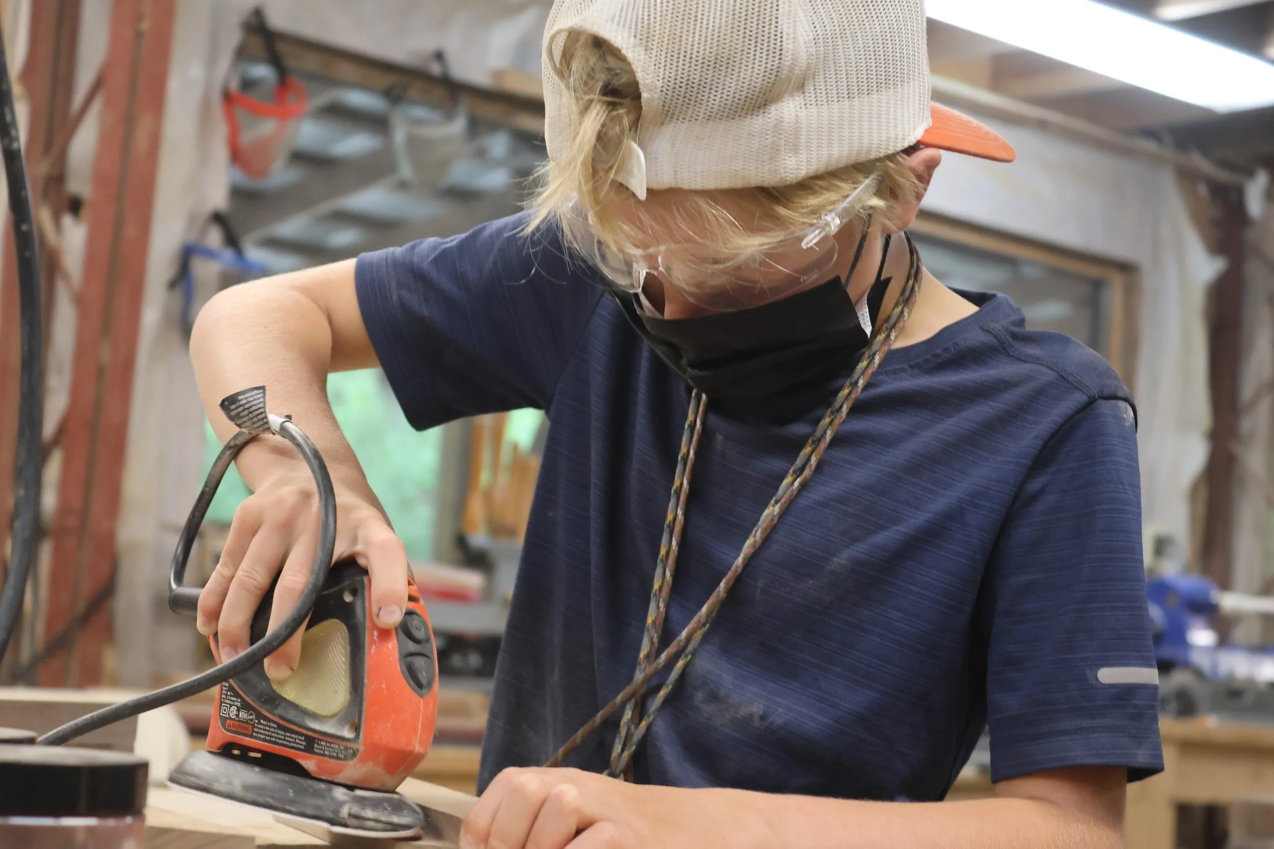 Camper uses power sanding tool to work on his woodworking project in the Arrowhead Woodshop. 