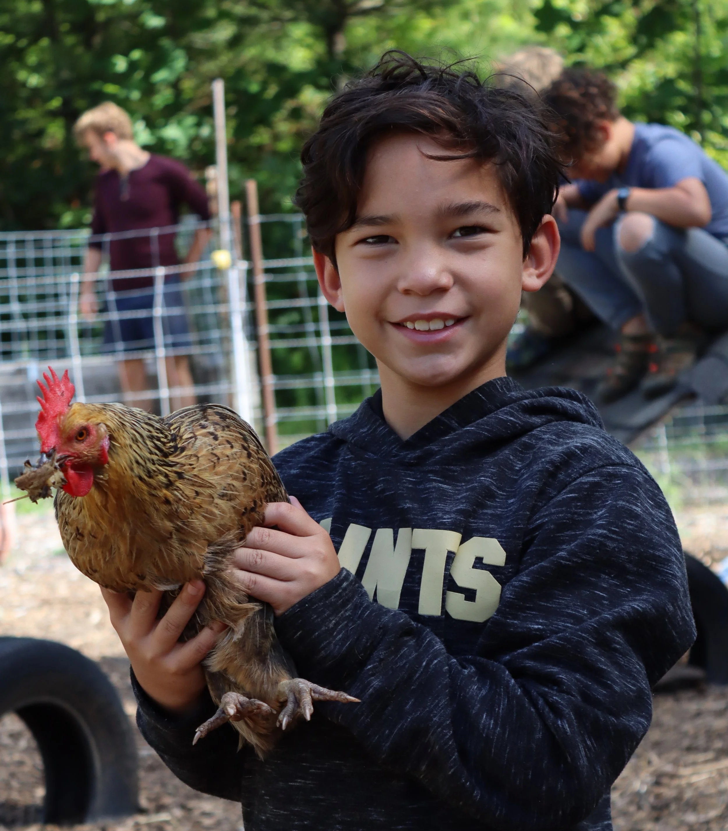 A Sleepaway camper holding a chicken, happy at Arrowhead for boys.