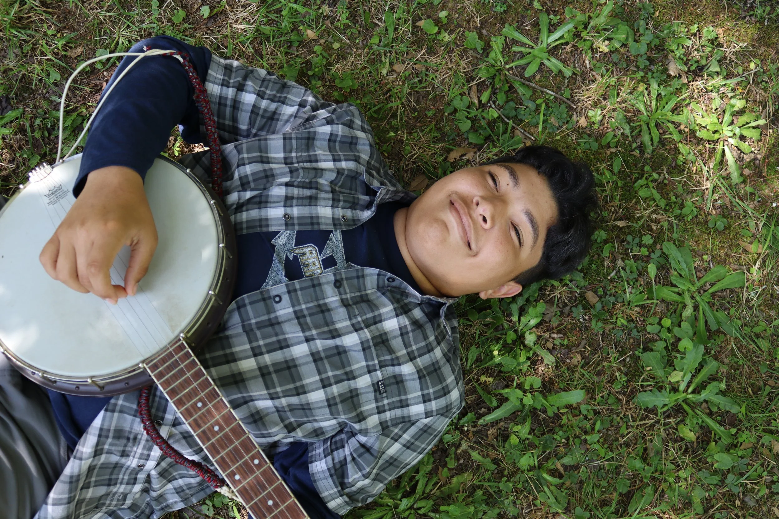 Arrowhead Summer Camper playing banjo while laying in the grass