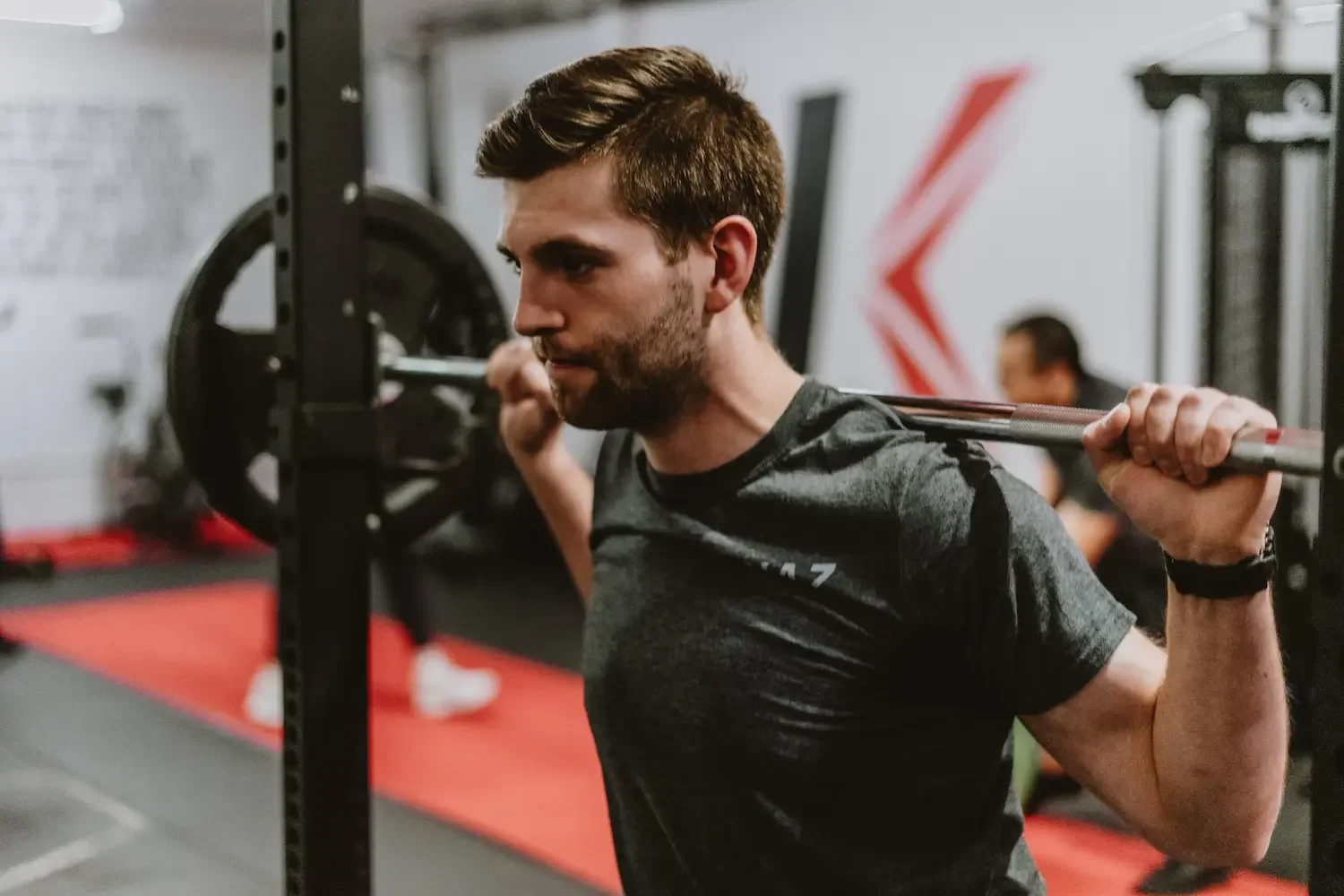 Man lifting a barbell across his shoulders while doing a squat in a gym.