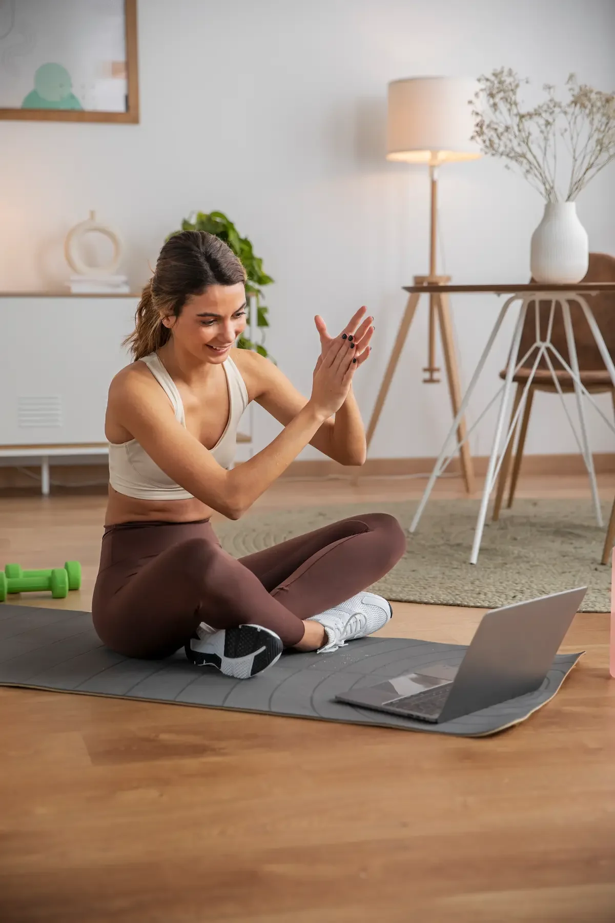 Woman in activewear doing a yoga or workout session on a yoga mat at home while following an online workout on her laptop.