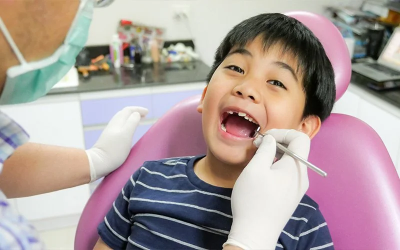 Young boy receiving routine dental examination in chair.