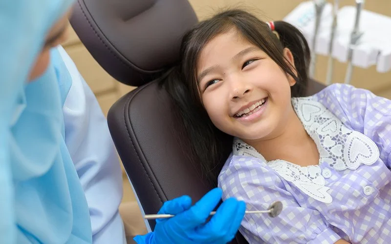 Pediatric dentist examining young patient smiling in dental chair.