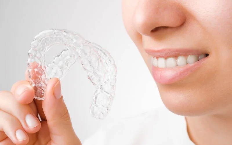 Patient holding clear aligners for bimaxillary protrusion treatment.