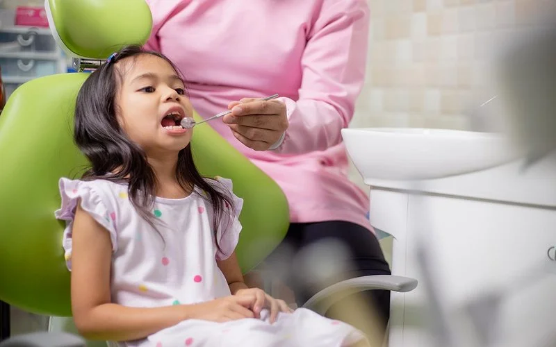 Dentist examining a young girl’s teeth at dental clinic.