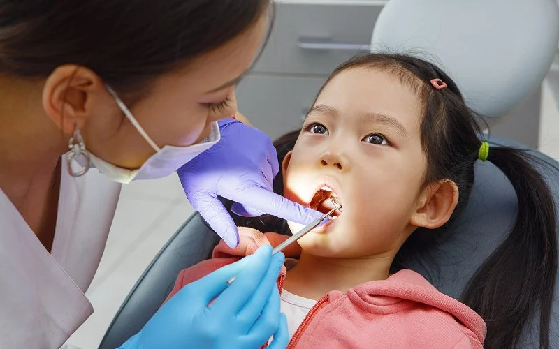 Dentist examining young girl's palate at a clinic.