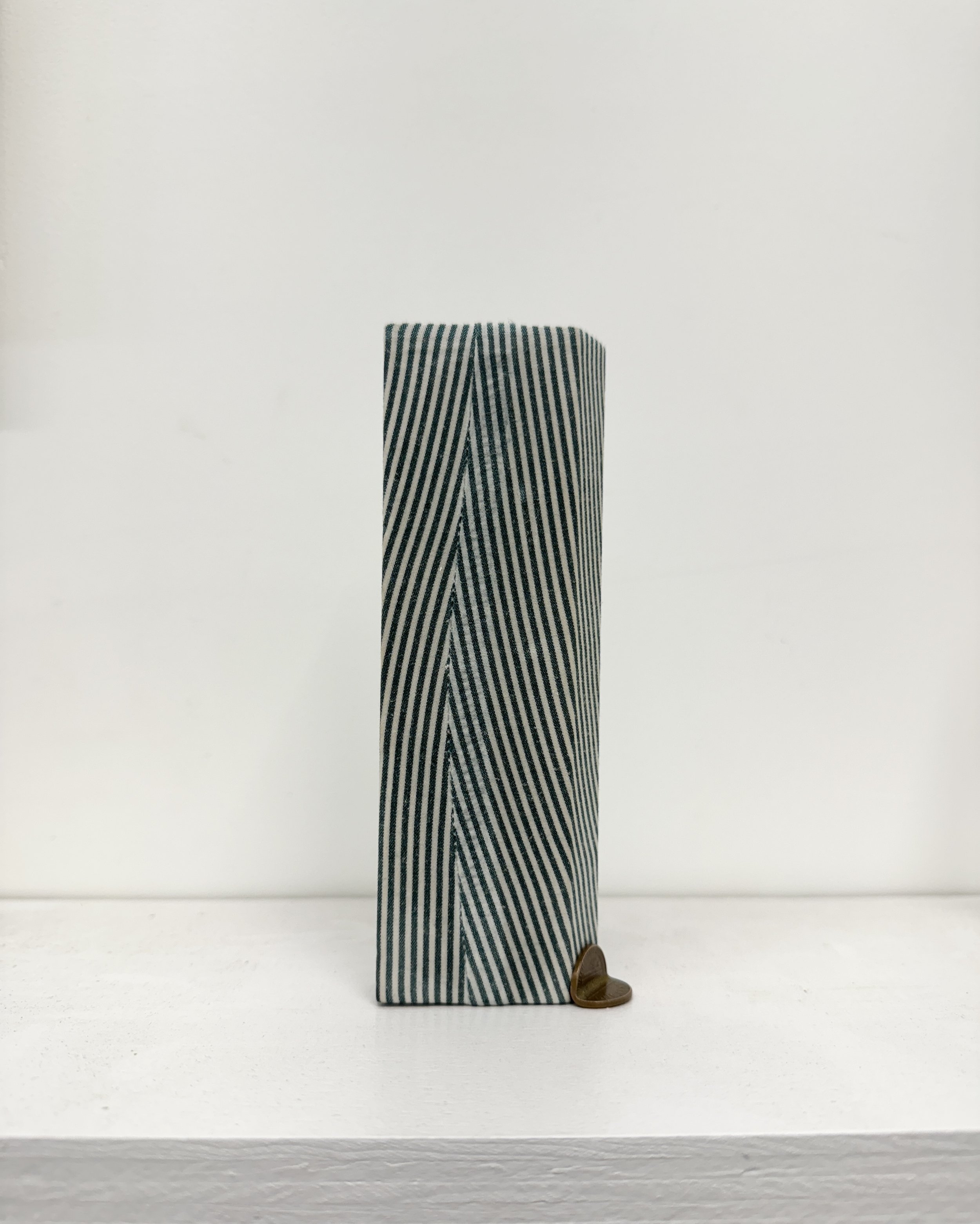 Eric Oglander, footing, 2025. Pine, fabric from button down shirt, beeswax, folded penny, 6 x 2 x 2 inches.