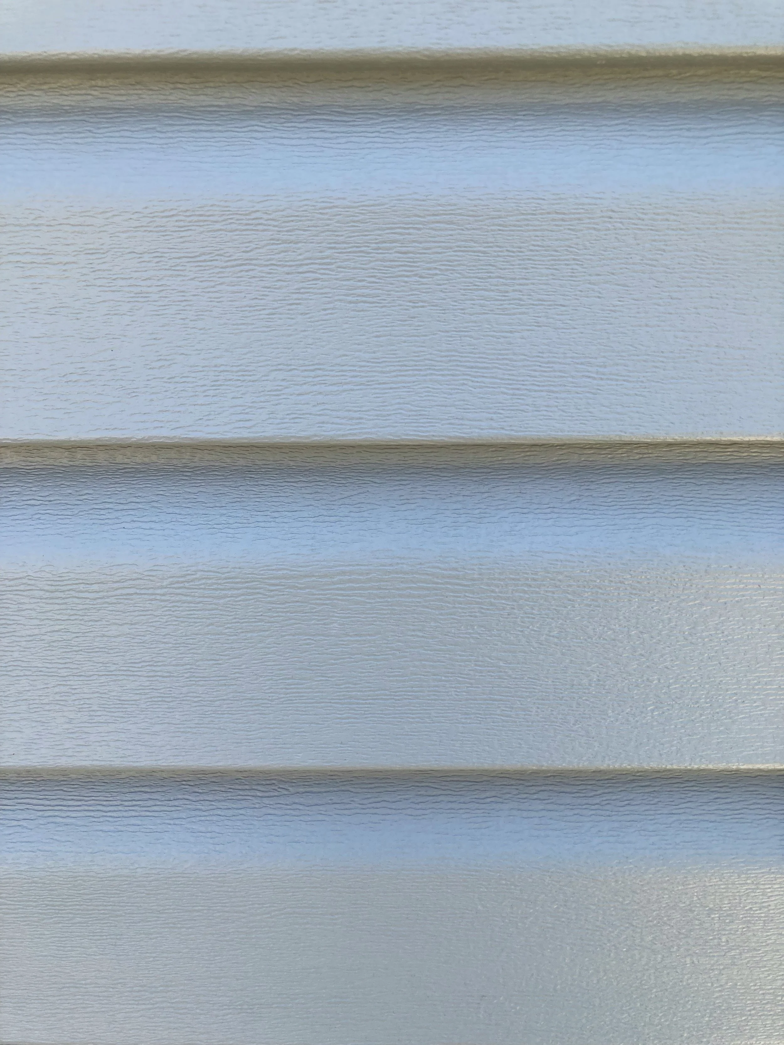 Close-up of light gray vinyl siding with horizontal ridges and textured surface.