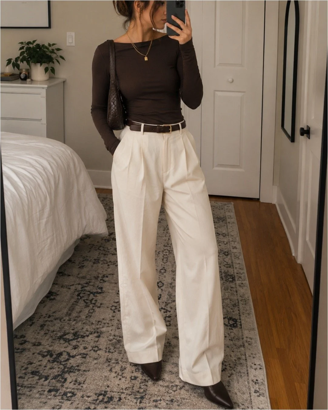 Trendy woman taking a mirror selfie in a classy outfit with cream trousers and a fitted brown top.