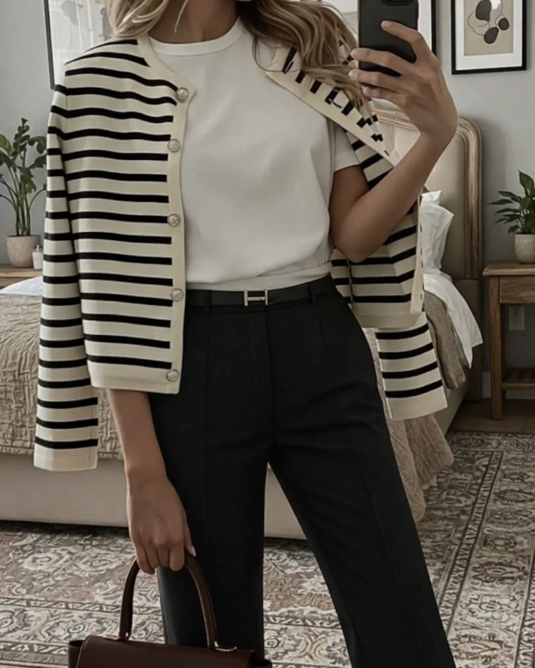 woman taking a mirror selfie in a stylish outfit with striped sweater and black pants
