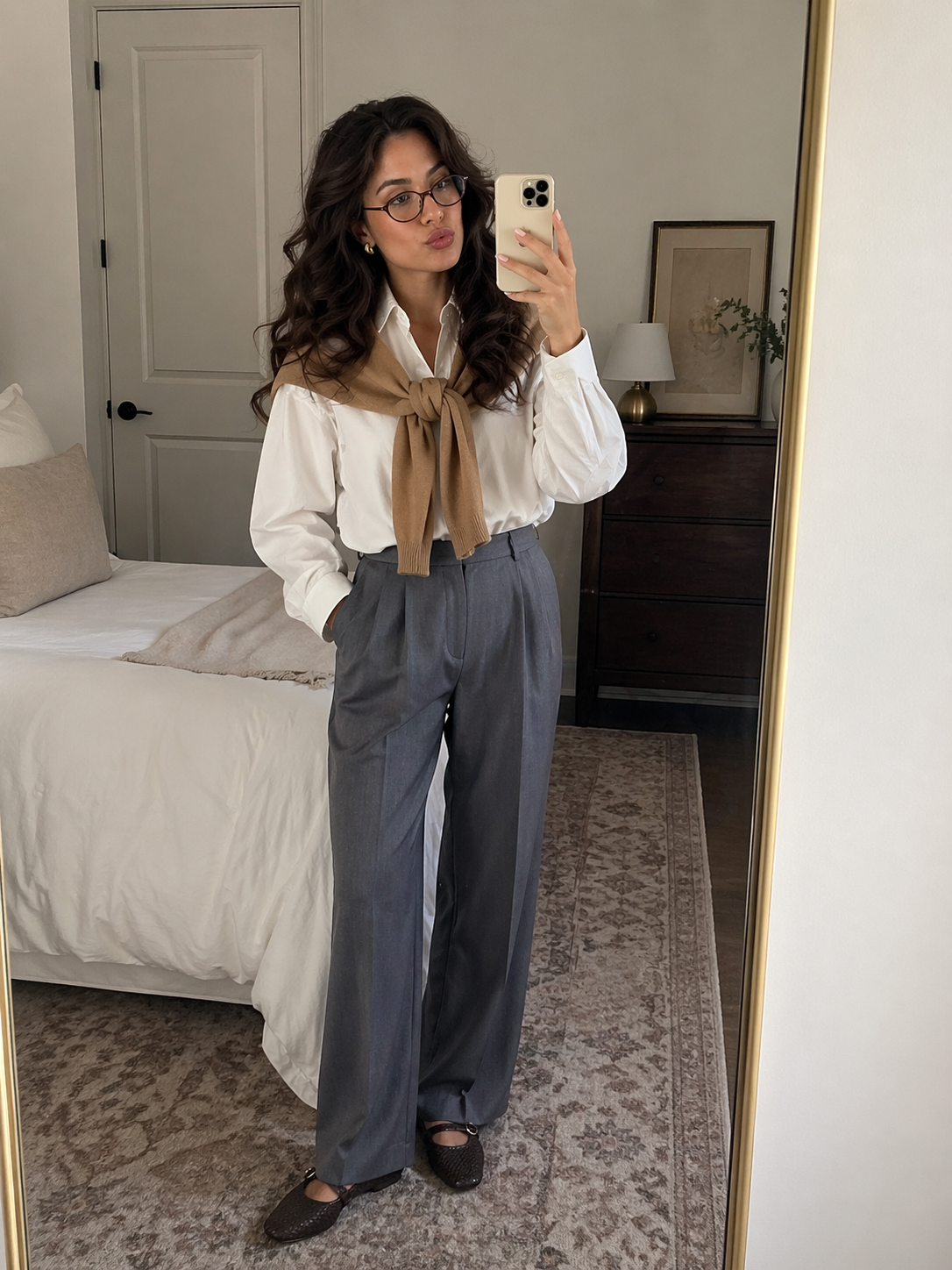 woman dressed nicely taking a mirror selfie in a bedroom