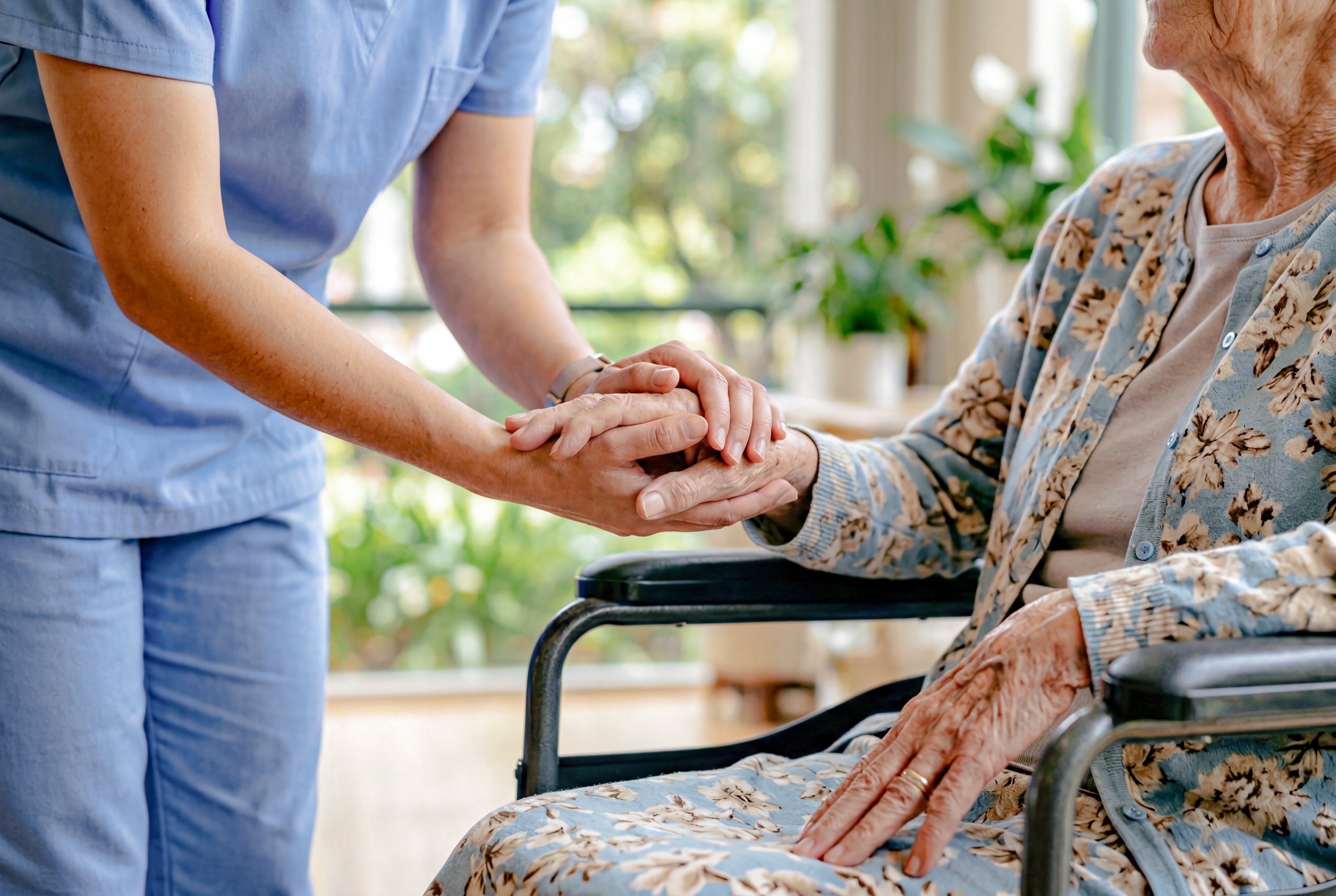 caregiver-holding-hands-elderly-woman-wheelchair.jpg