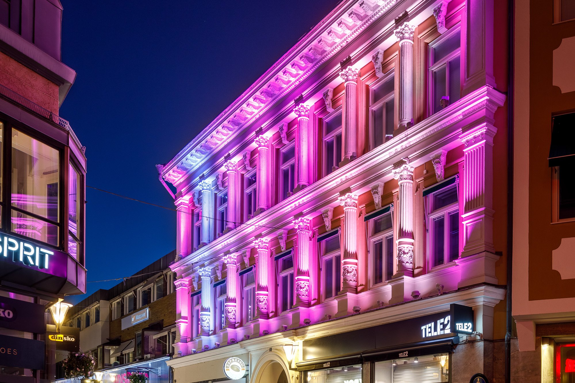 Vacker fasadbelysning antikinspirerad byggnad i Linköping med färger från rosa till blått