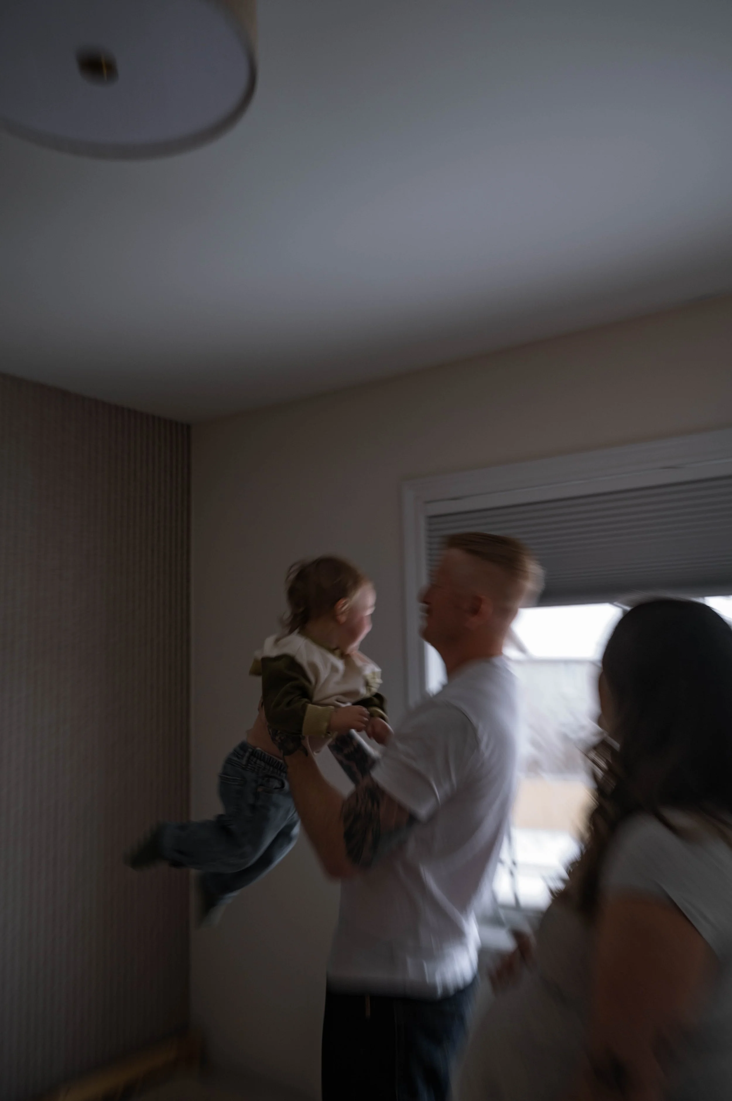 A blurry, moving image of a dad picking his toddler up to throw him in the air, while pregnant mom looks on. During a lifestyle in-home maternity session.