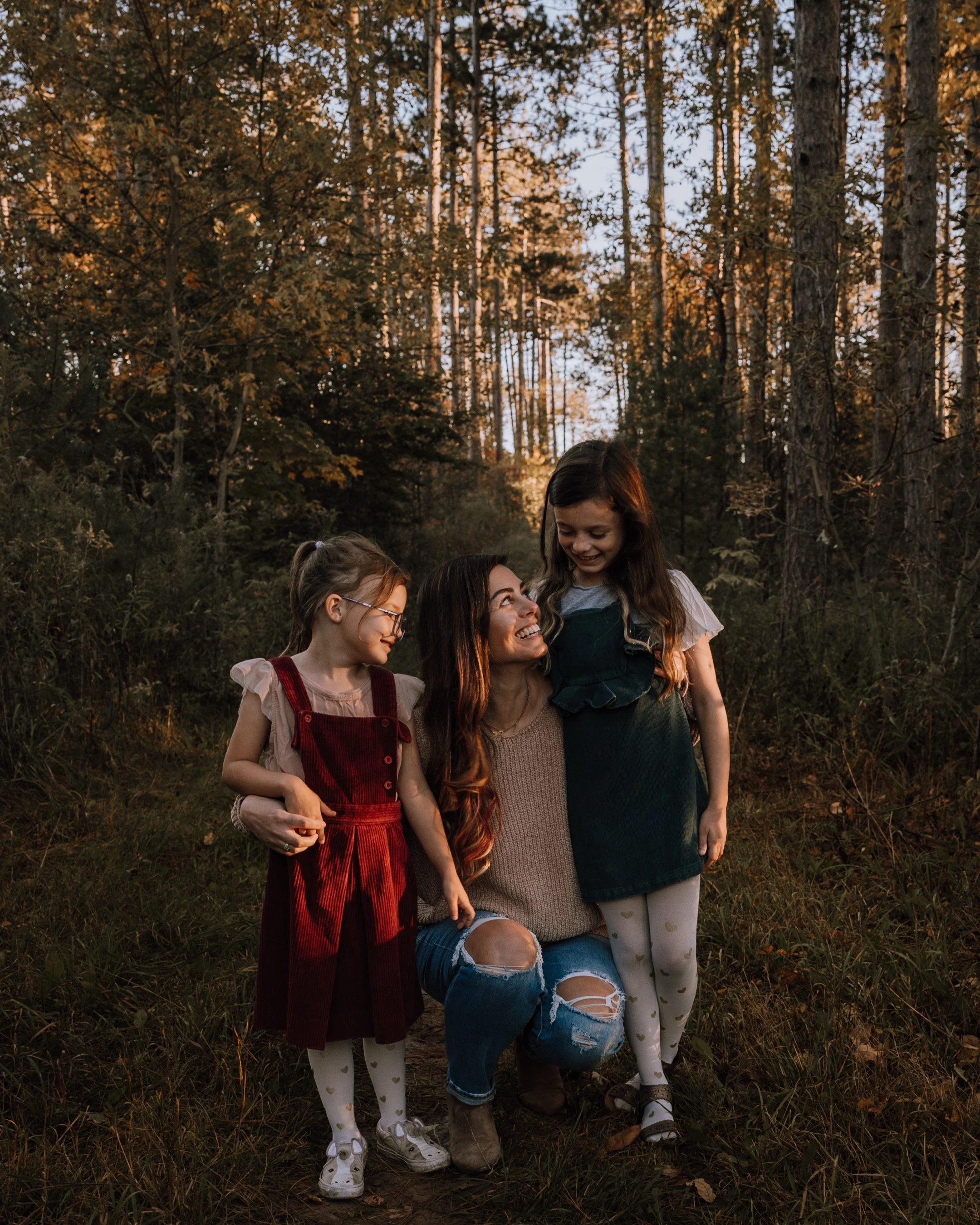 Aurora family photographer Mia Purdy smiling with with and looking adoringly at her two daughters on a trail in Newmarket.