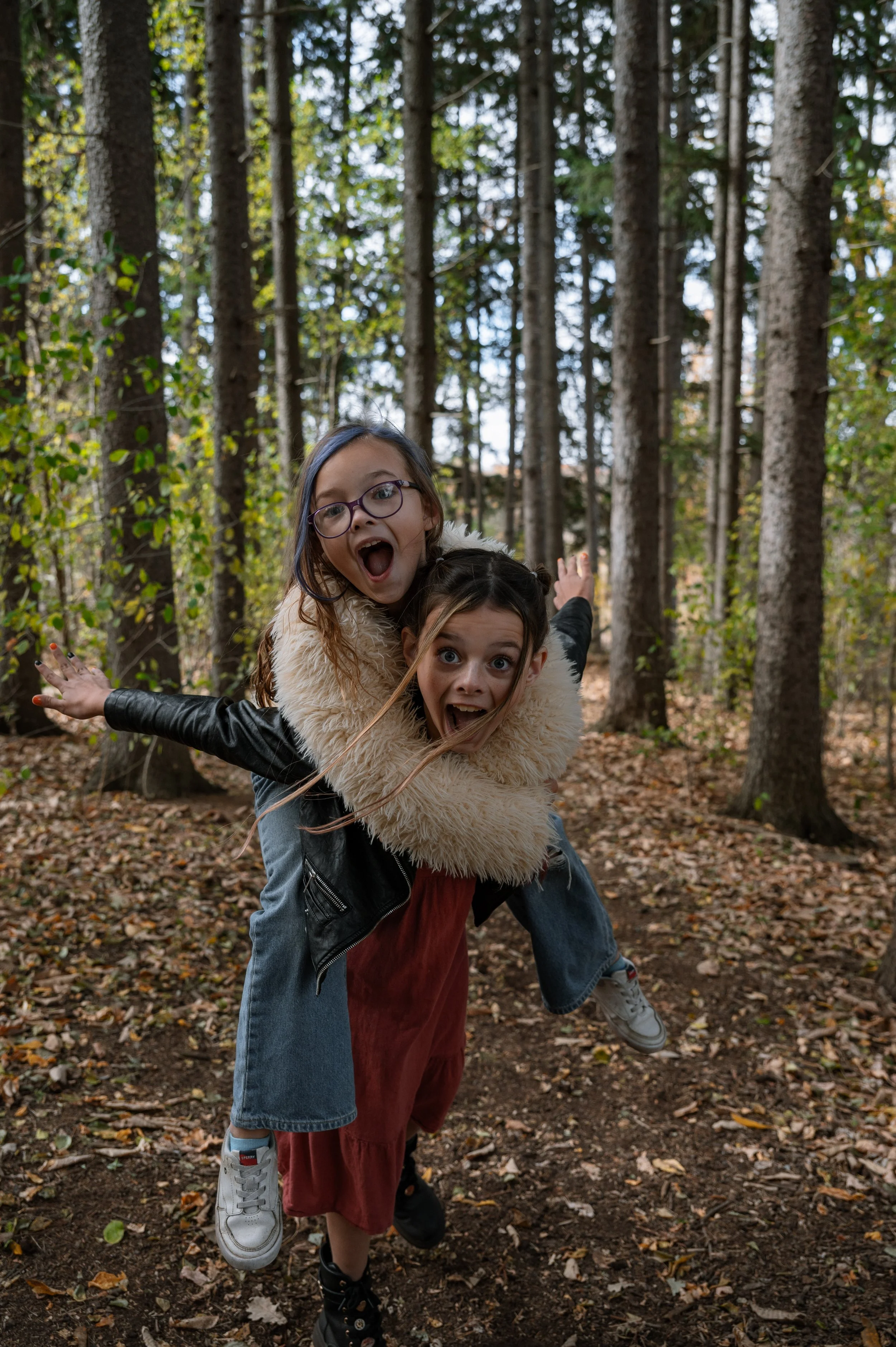 A younger sister getting a piggy back ride from her elder sister and both making excited, dramatic faces during a family photo session in Aurora, Ontario.