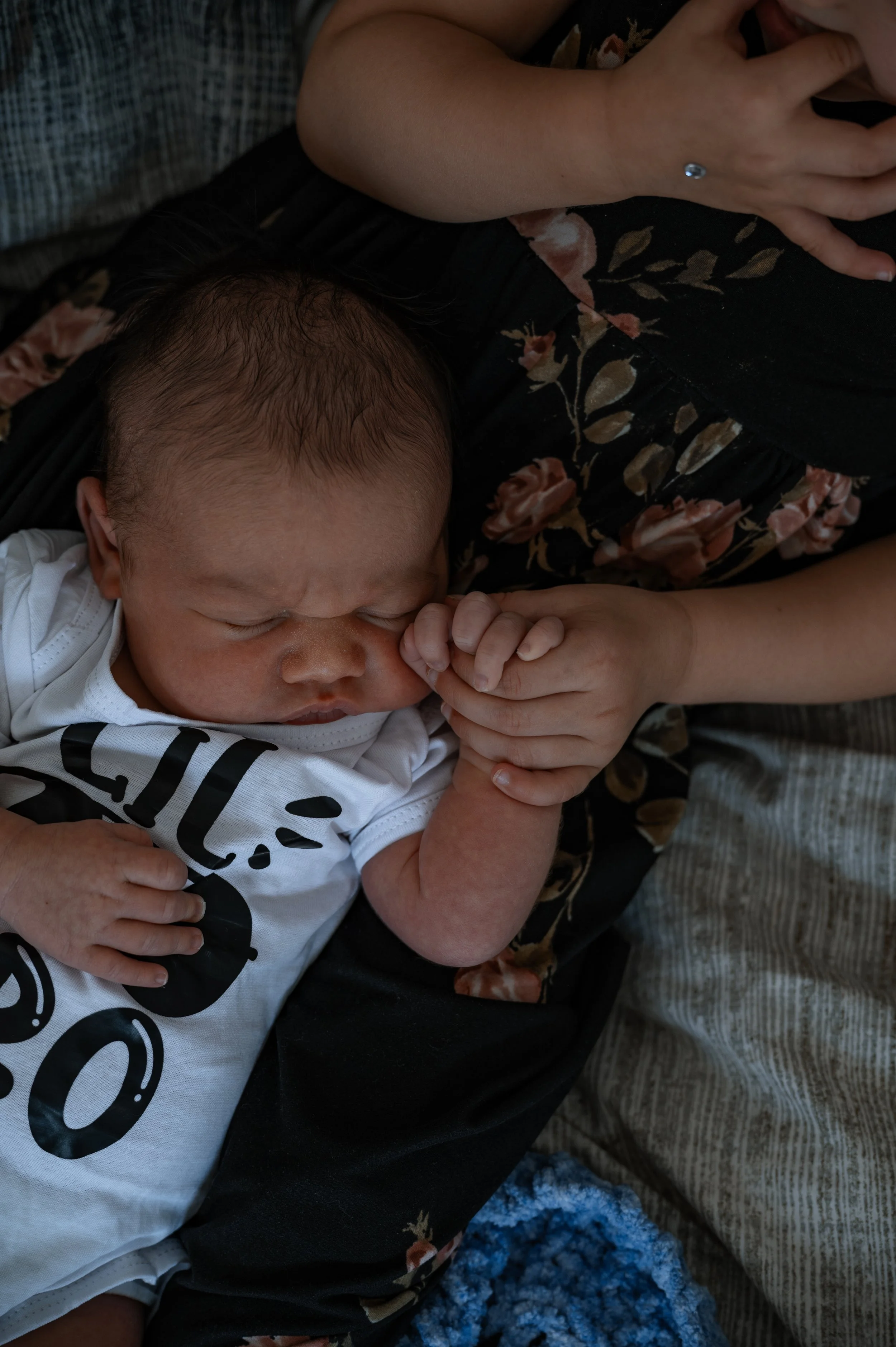 A newborn baby cuddled up with older sibling who is holding his hand, during an in-home newborn session.