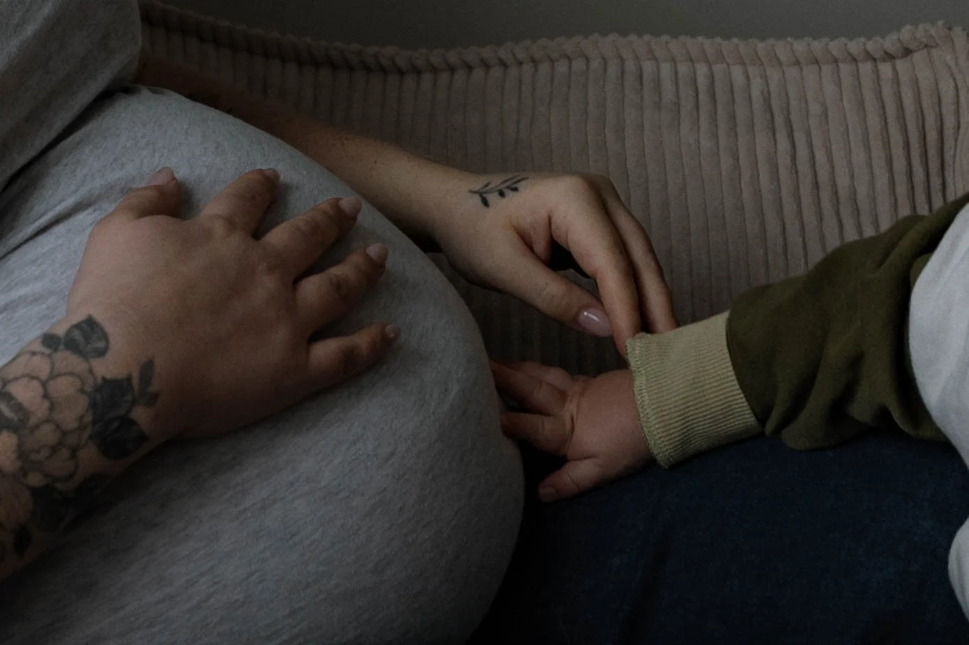 Close up of a toddler’s hand and mother's pregnant belly during a cozy in-home lifestyle maternity session.