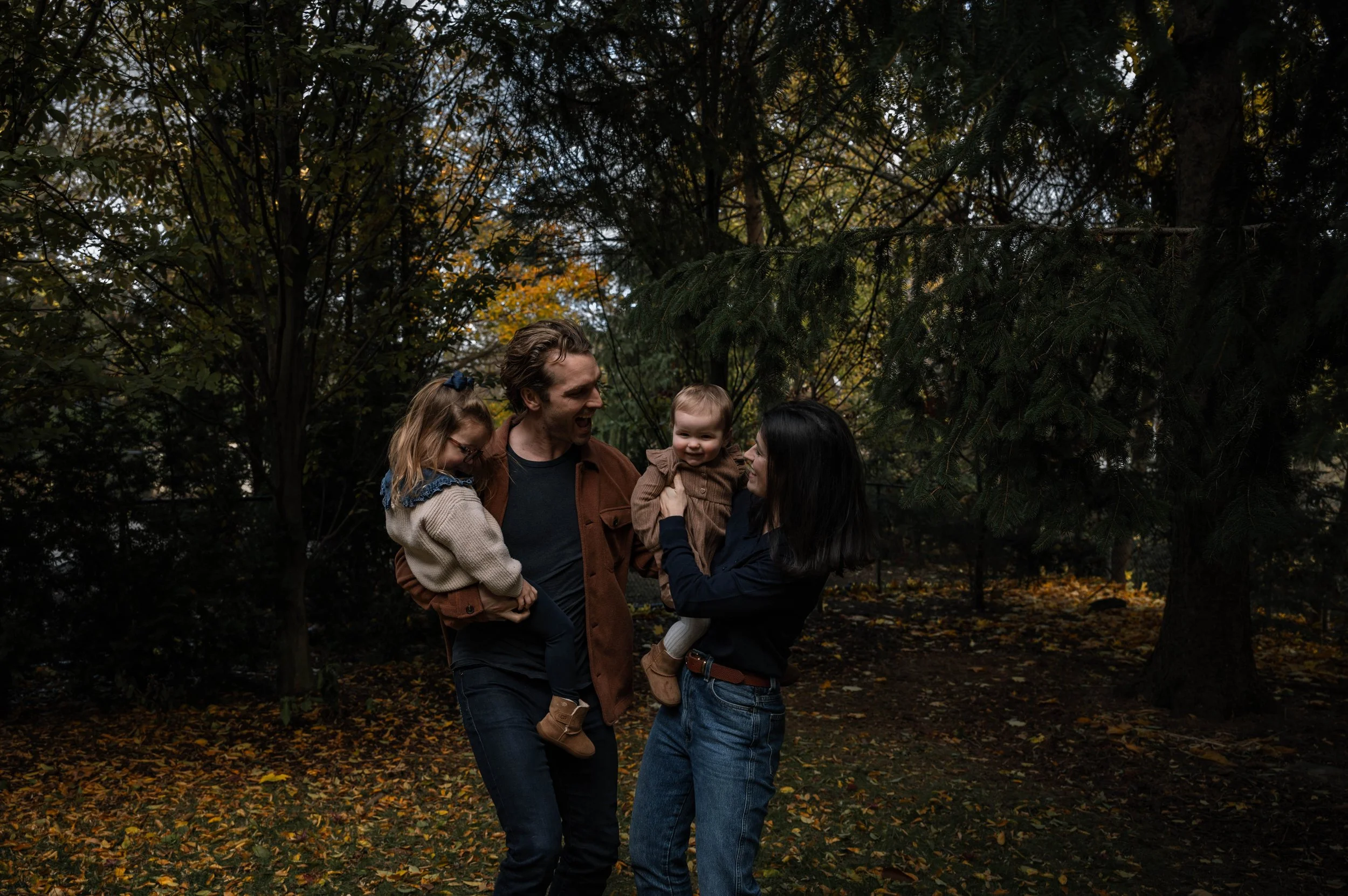 A colourful photo of parents holding their two daughters and all laughing together during a home family session in Oakville, Ontario.