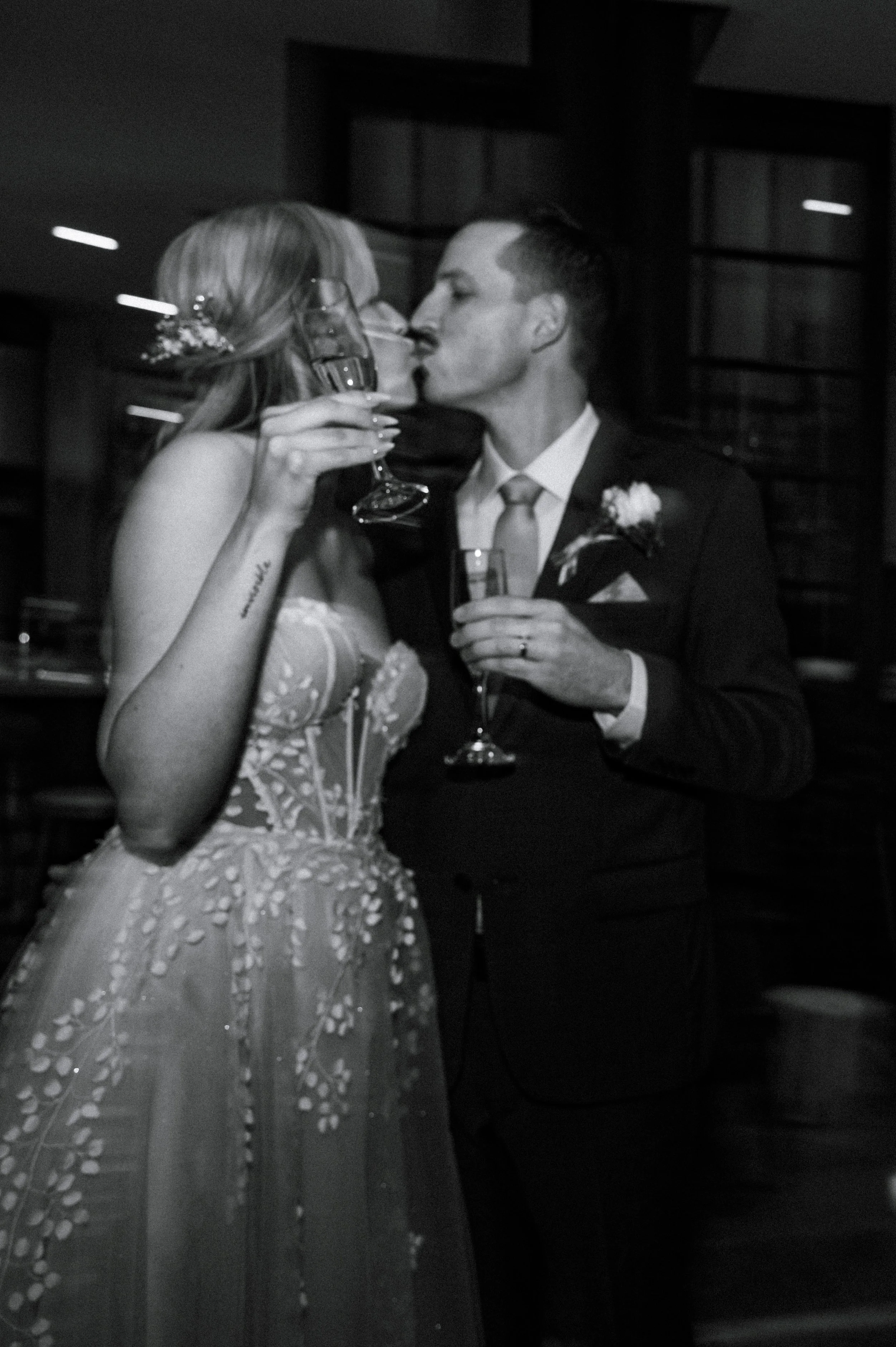 A bride and groom kissing while holding champagne during their wedding celebration in Newmarket, Ontario.