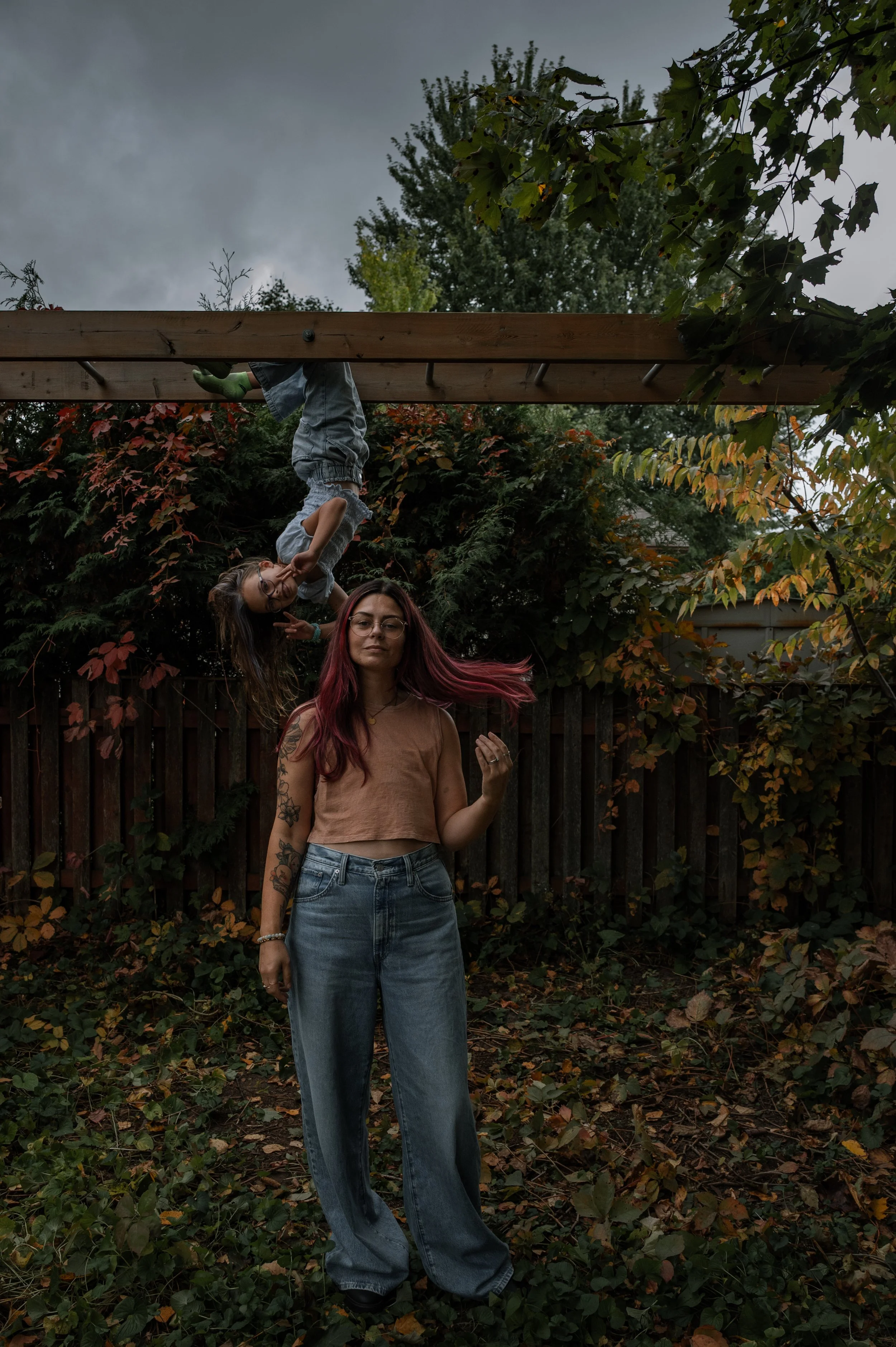Newmarket family photographer Mia Purdy tossing her hair behind her, while her daughter hangs from monkey bars behind her in Aurora, Ontario.