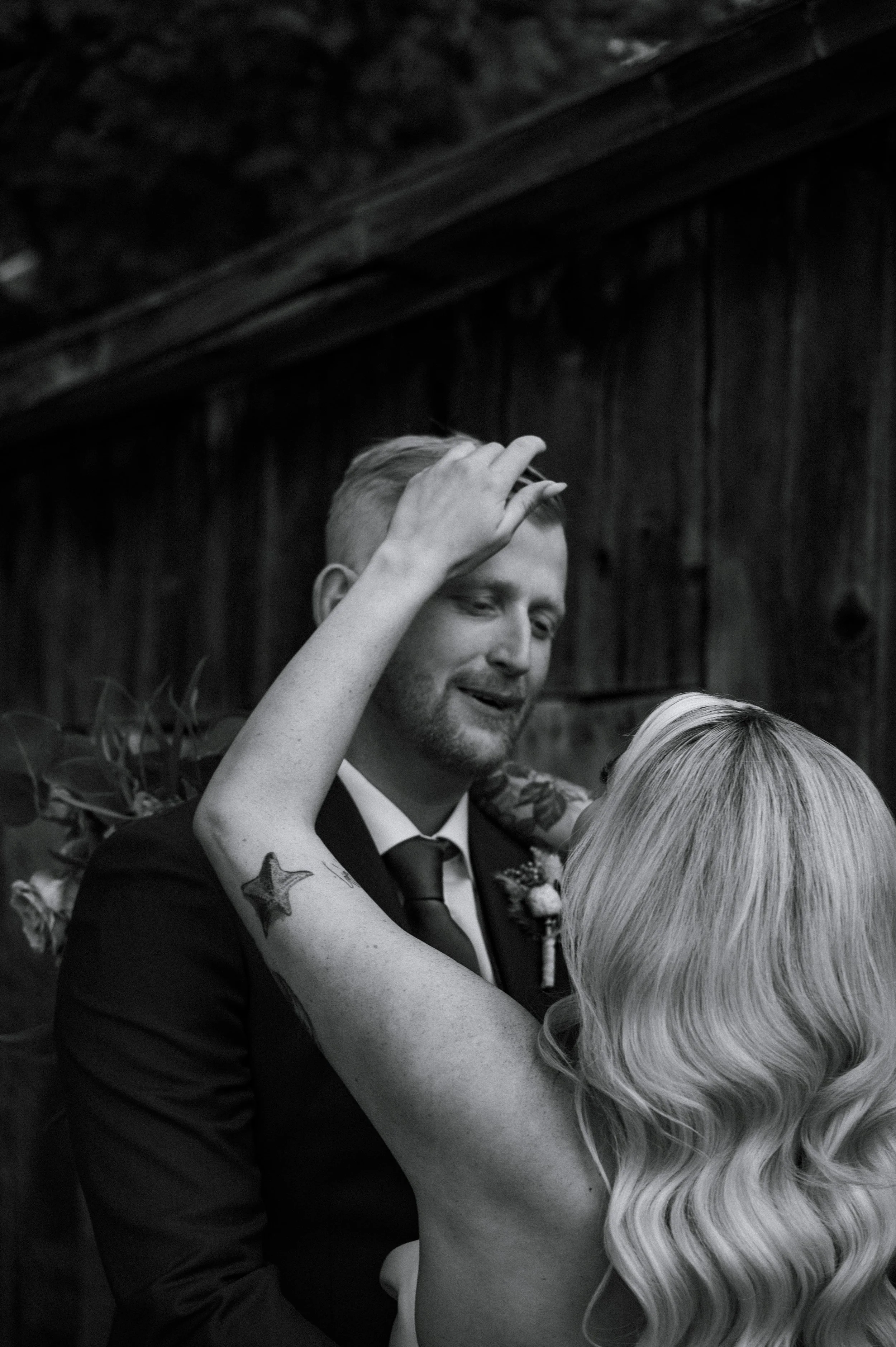A candid black and white portrait of a bride reaching up to fix her groom's hair, as he looks down at her lovingly, during their wedding in York Region, Ontario.
