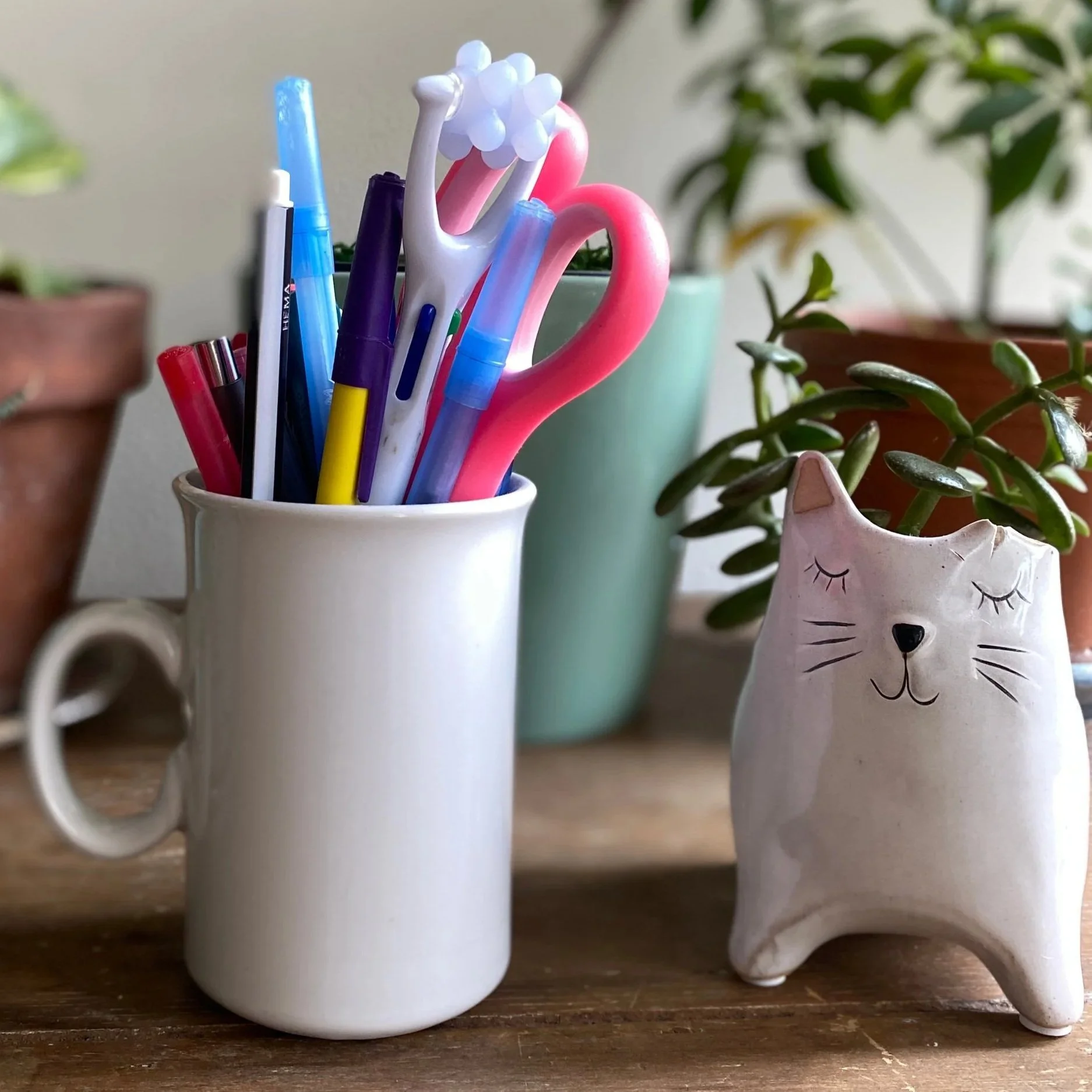 Mug holding colourful office supplies and a vase shaped like a cat