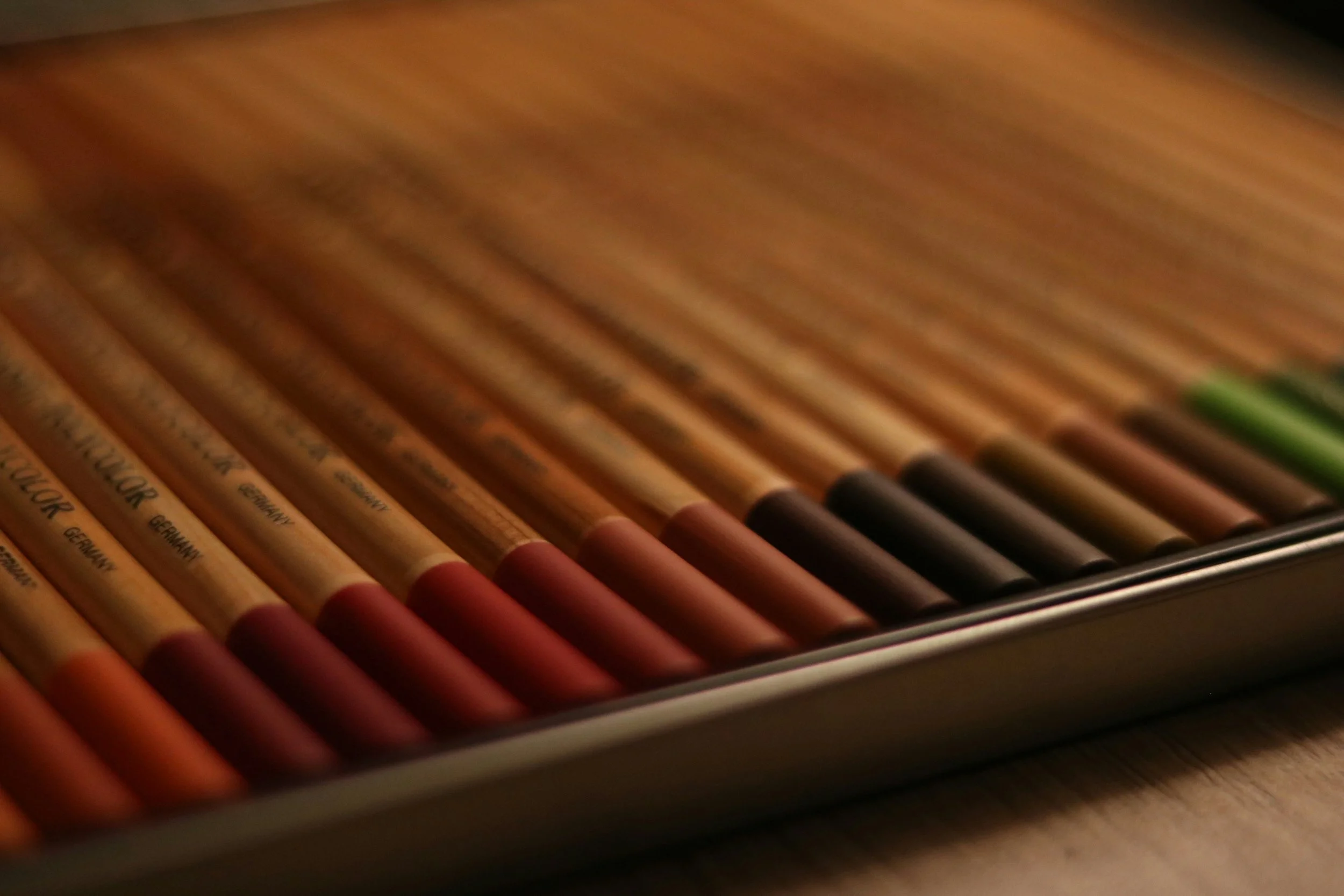 A set of coloured pencils in warm, earthy hues on top of a wooden table.