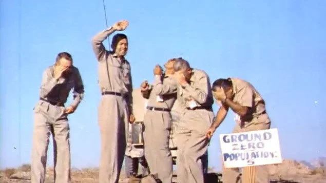 Five Air Force officers and one cameraman stand at ground zero, under an exploding nuclear weapon.