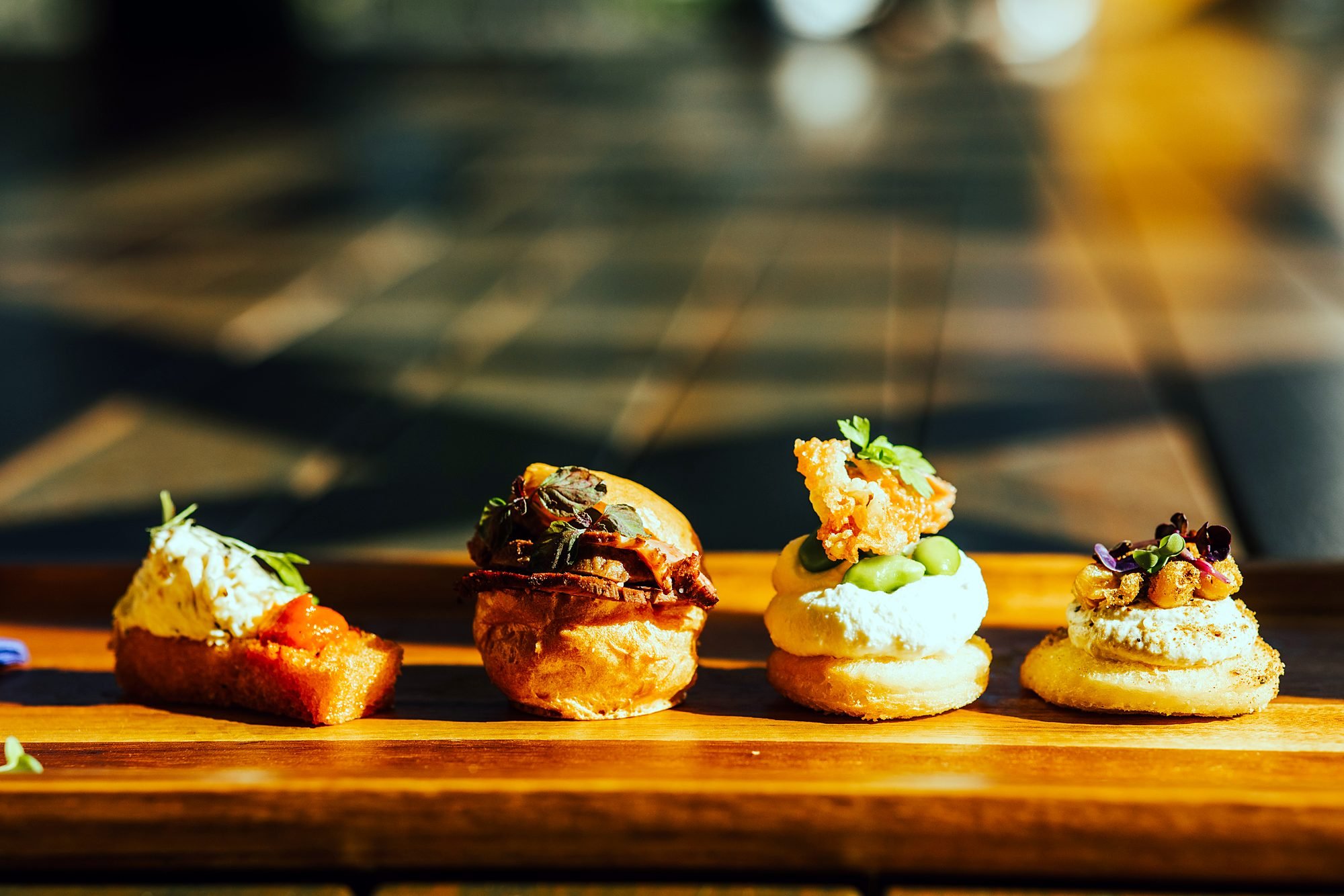 Row of gourmet slider canapés on a wooden serving board