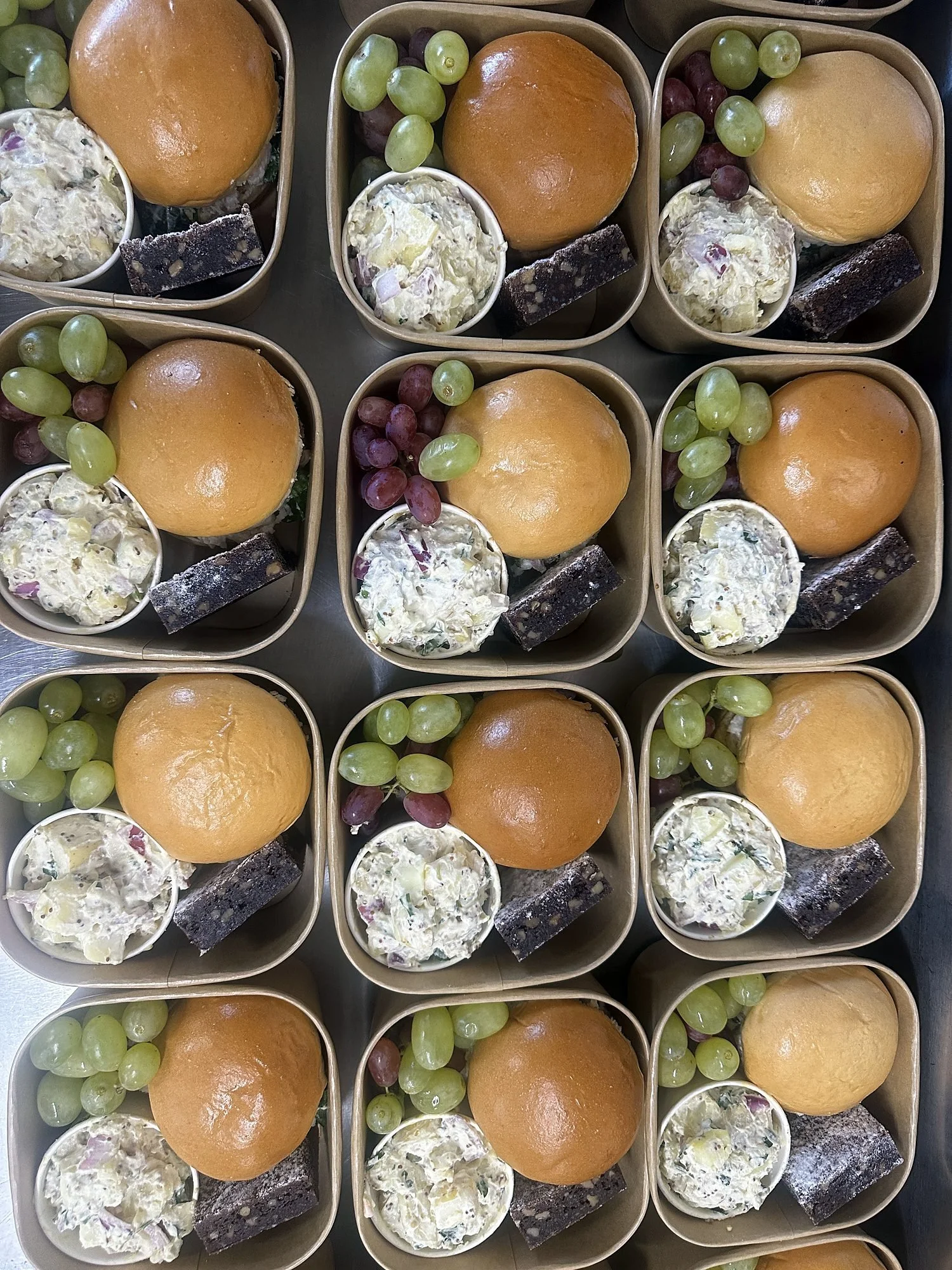 Individual lunch boxes with rolls, grapes and salad