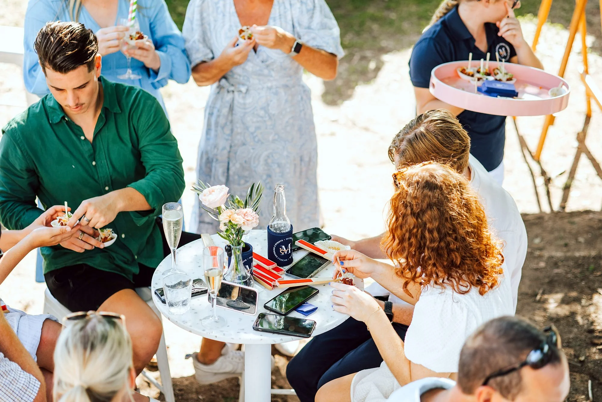 Friends sharing canapés and drinks around a table at an outdoor celebration