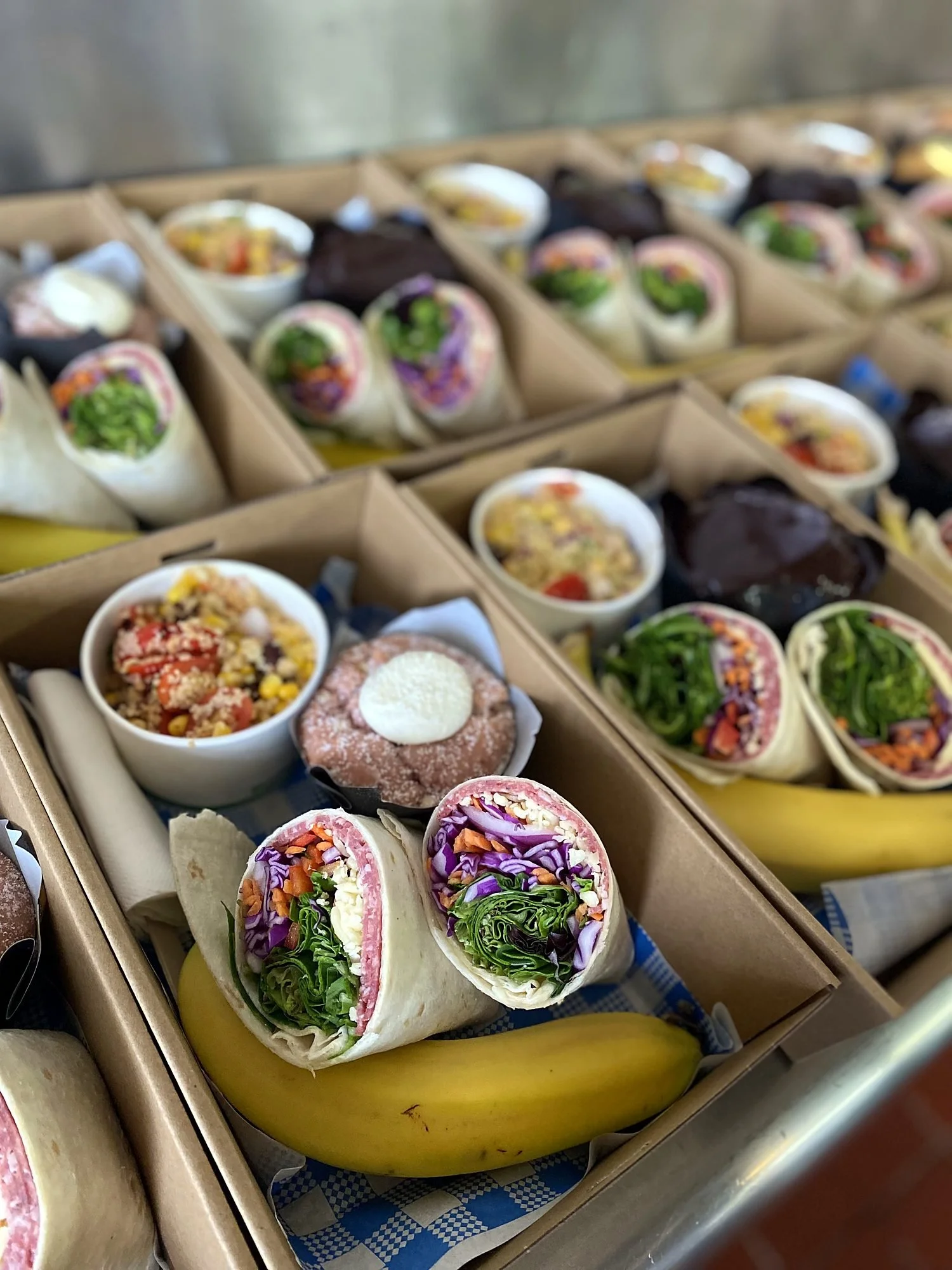 Individual lunch boxes with wraps, salads, a muffin and fruit, ready for delivery