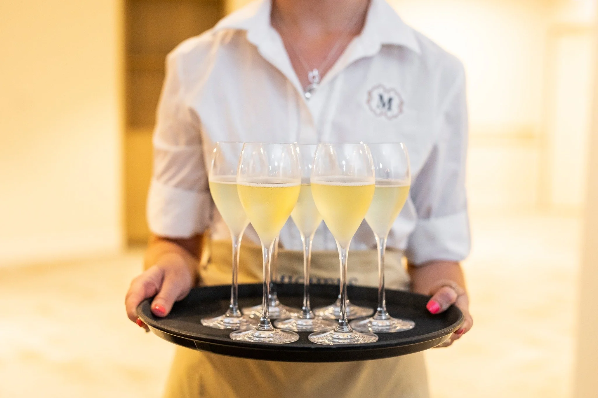 Person in white shirt holding a tray with multiple glasses of white wine.