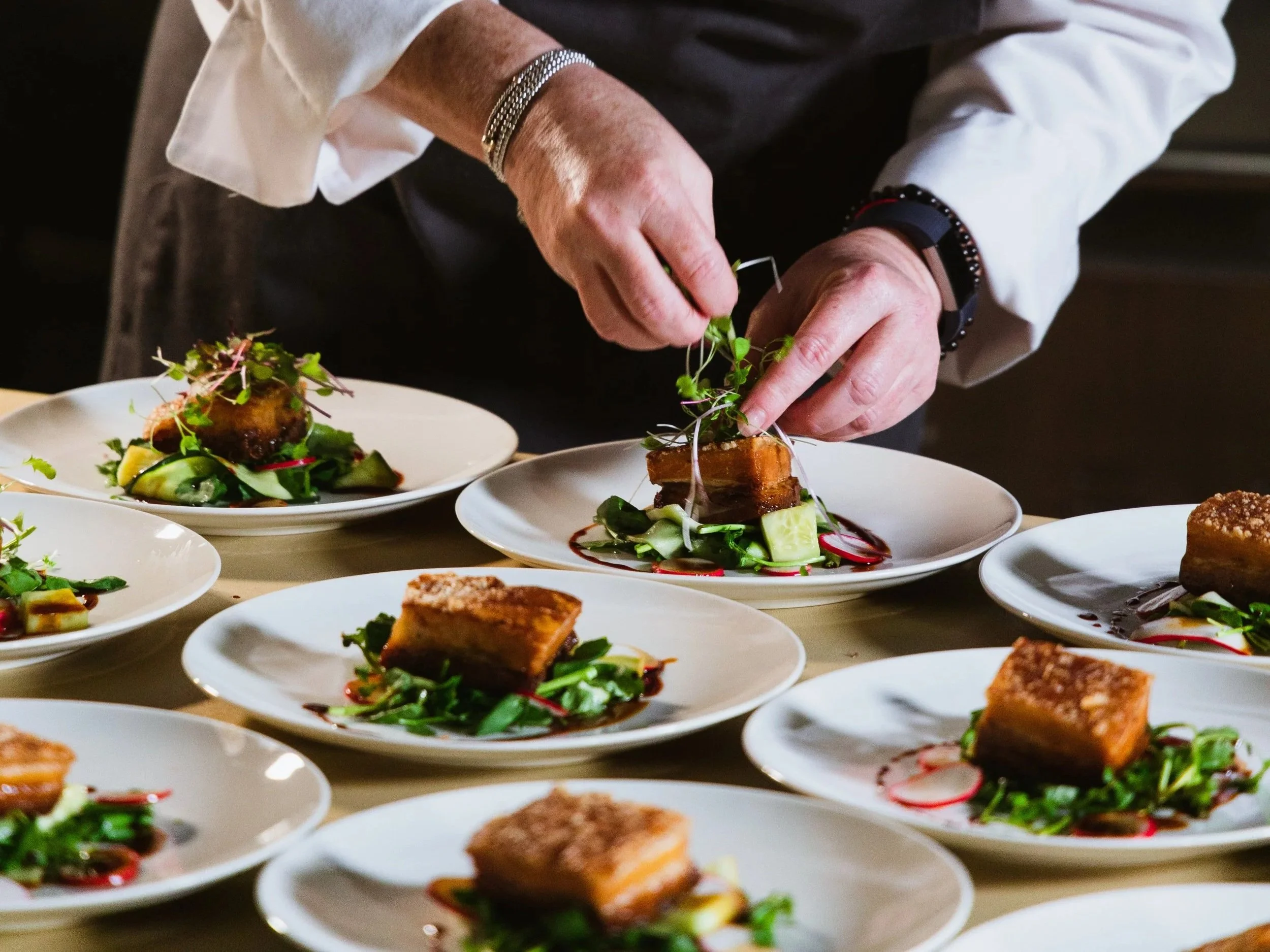A chef decorates gourmet plates with microgreens in a professional kitchen.