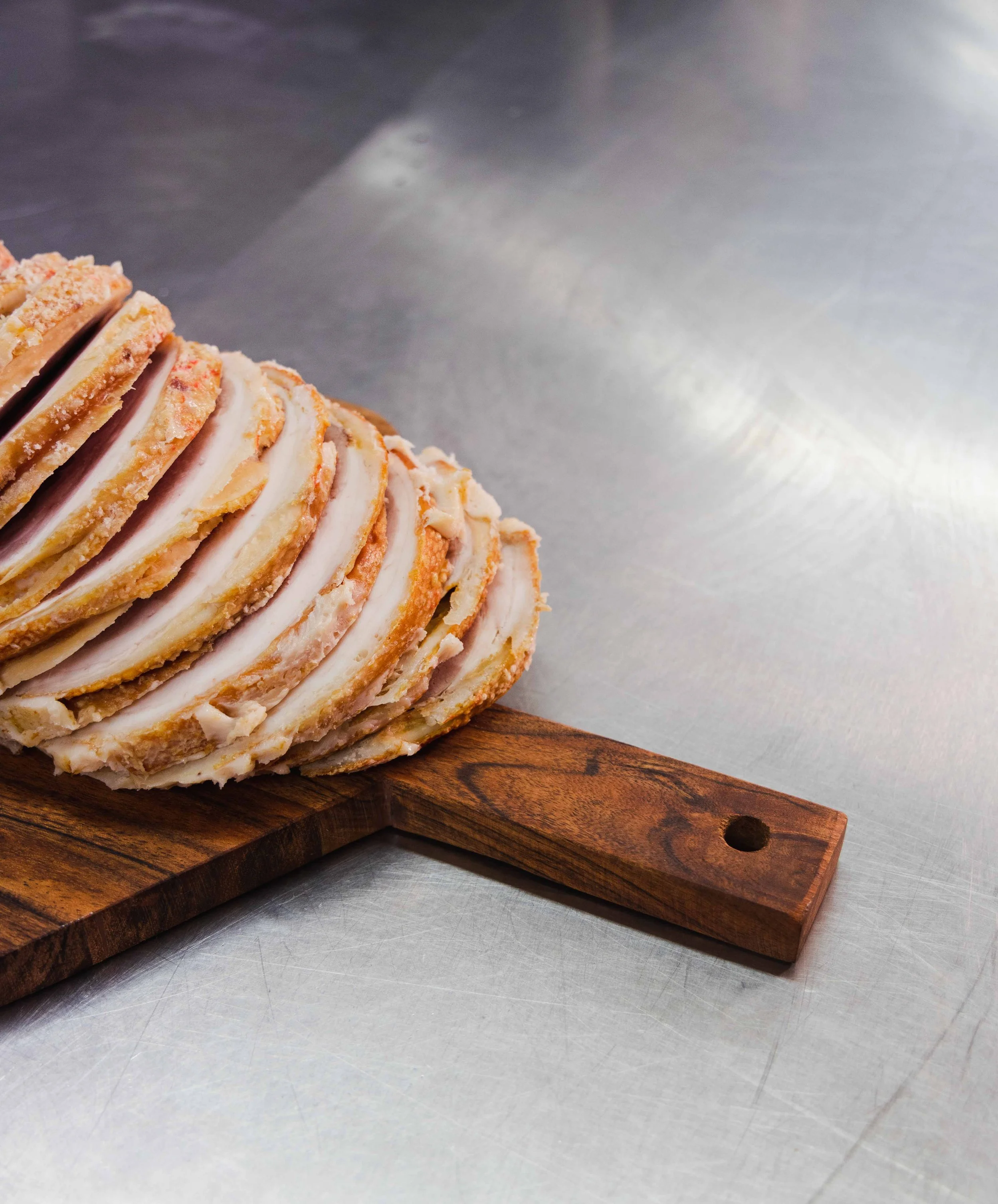 Sliced layered cake with white frosting and orange crumbs on a wooden cutting board on a metallic surface.