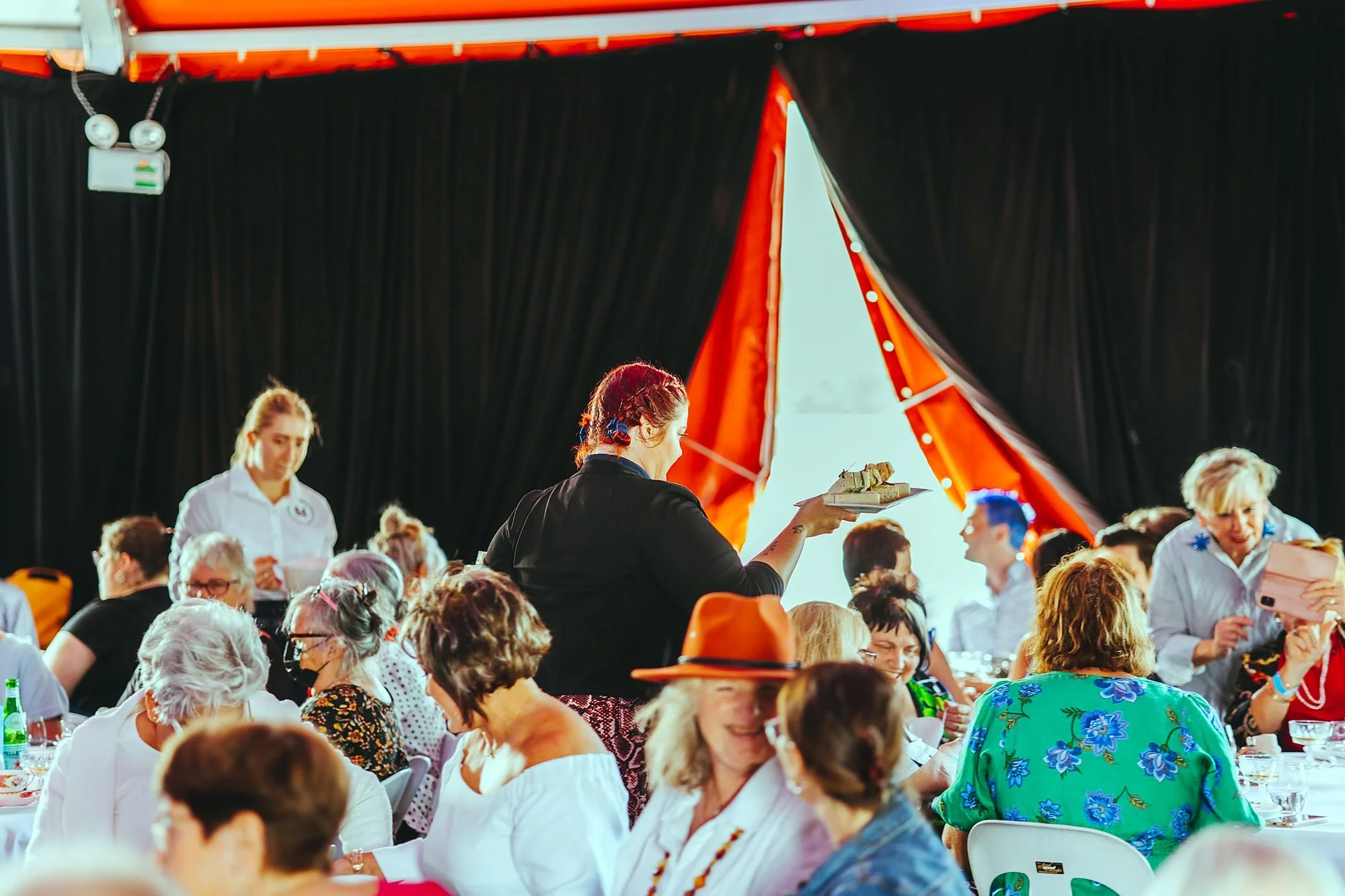 Guests dining under a red and white marquee at an evening event with live music