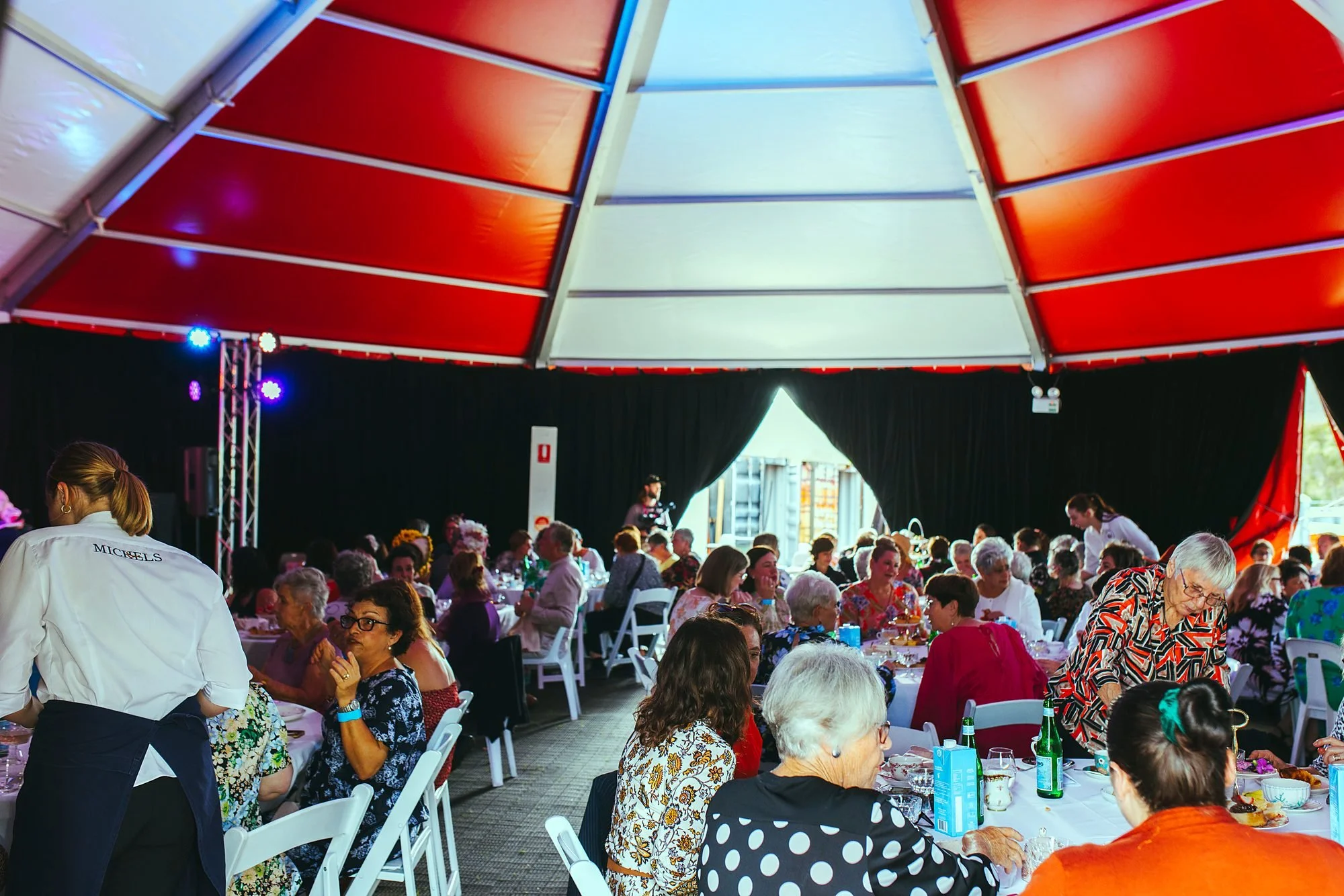 Hundreds of guests dining in a large red marquee while Michels staff serve