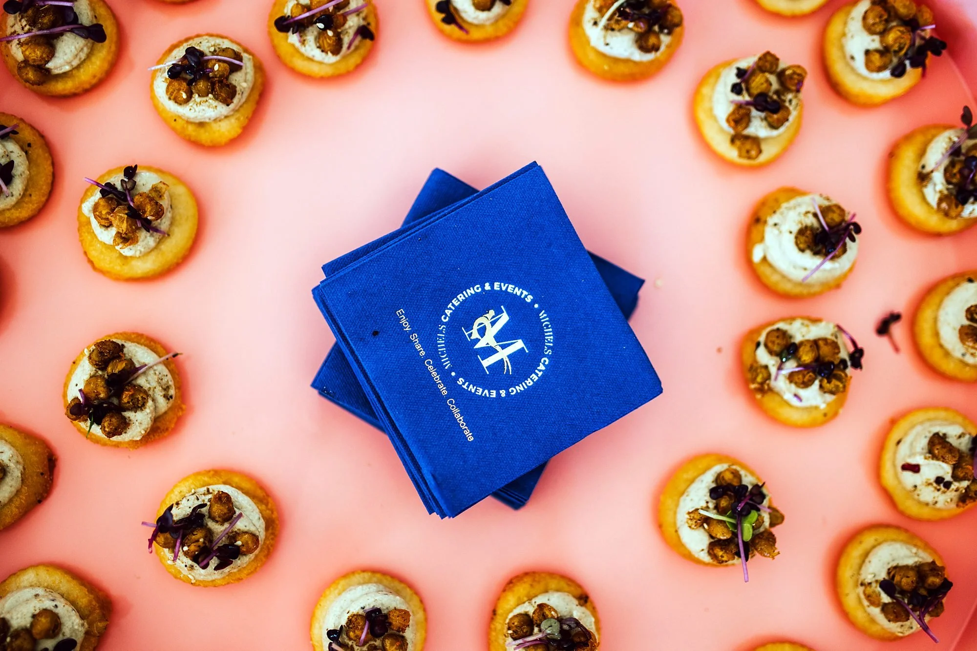 Canapés arranged around Michels branded napkins on a pink background