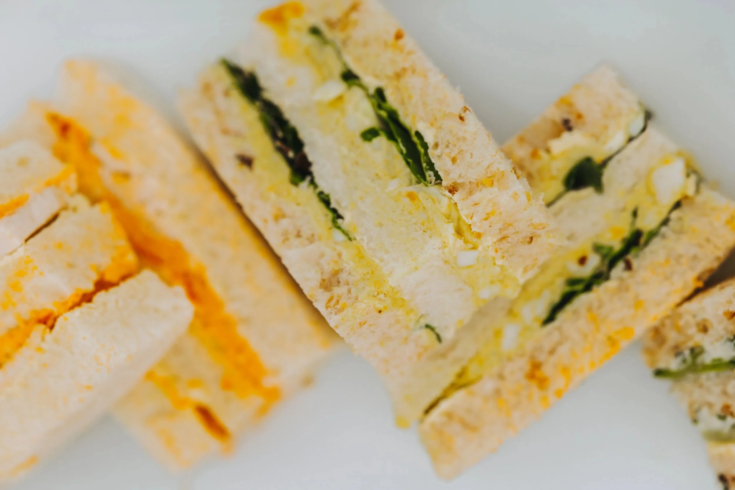 Close-up of a layered sandwich with lettuce, cheese, and possibly egg salad, cut into rectangular pieces.